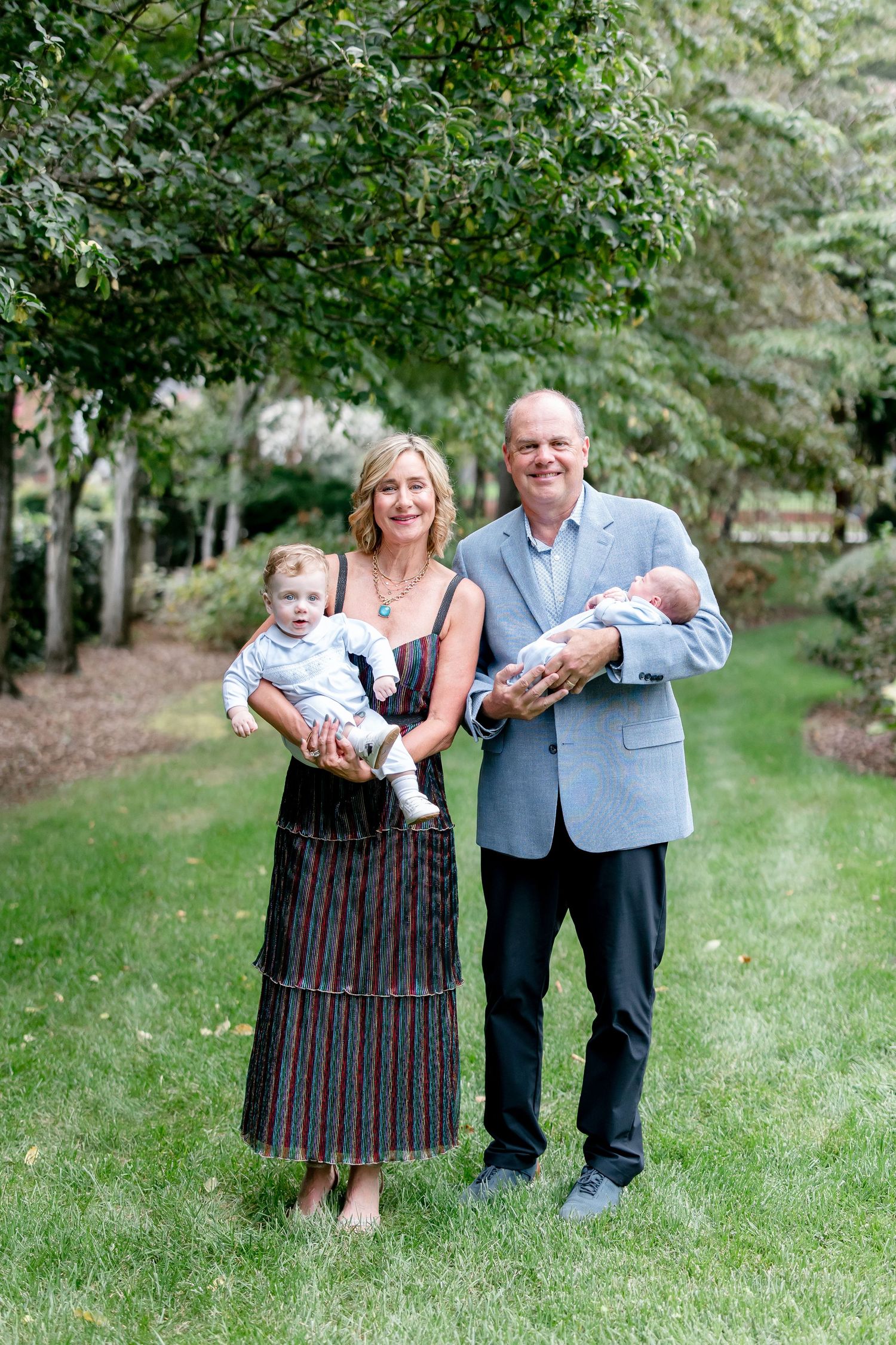 A family portrait series taken outdoors with lush greenery and trees in the background.