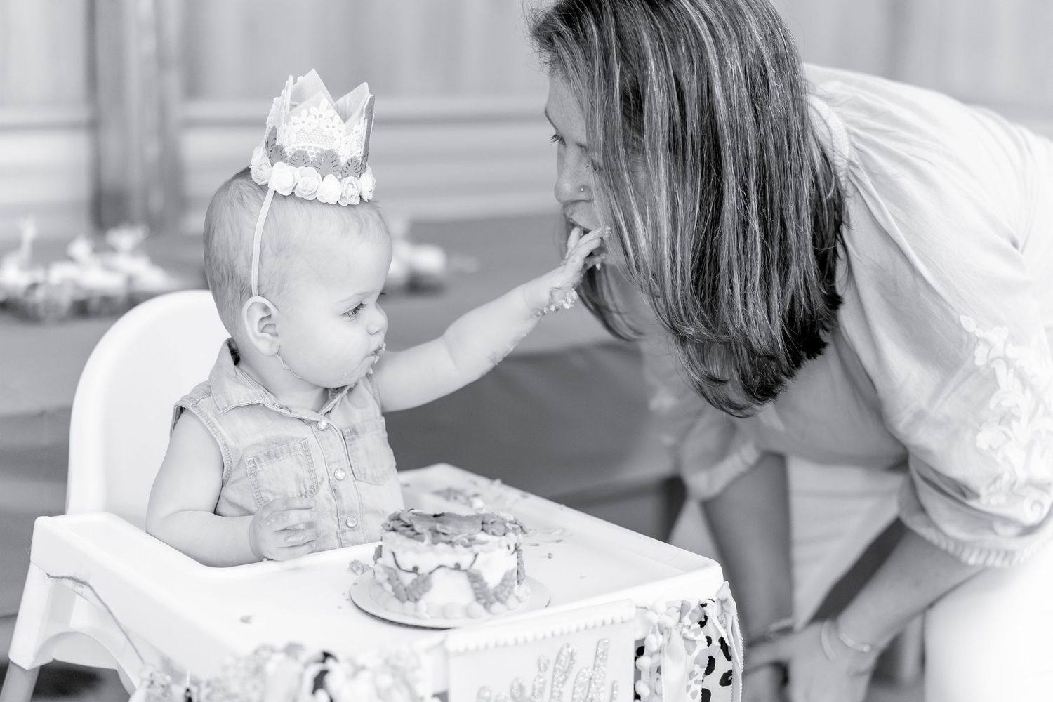 Black and white photo of celebration with baby in high chair wearing crown.