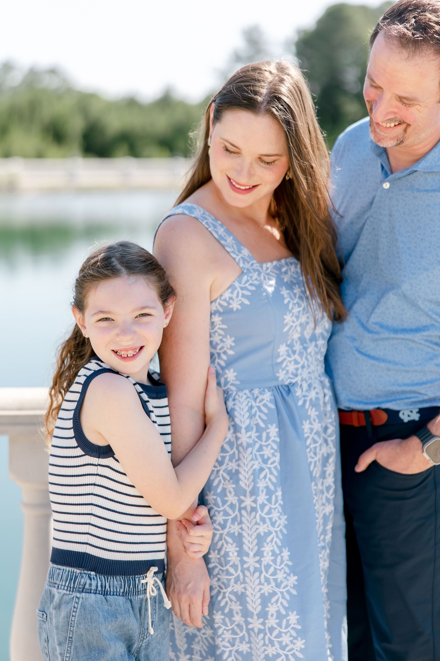 Candid moments of a family sharing laughter and embraces while posing on lakeside balcony in blue attire.