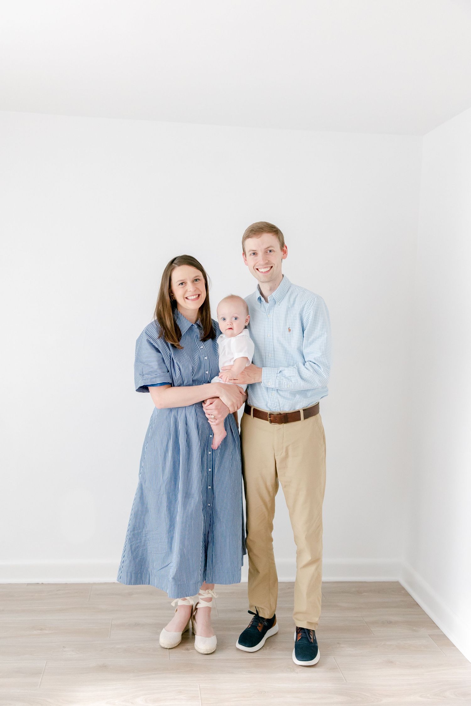 A family in coordinated blue and khaki outfits poses together in a minimalist white room.