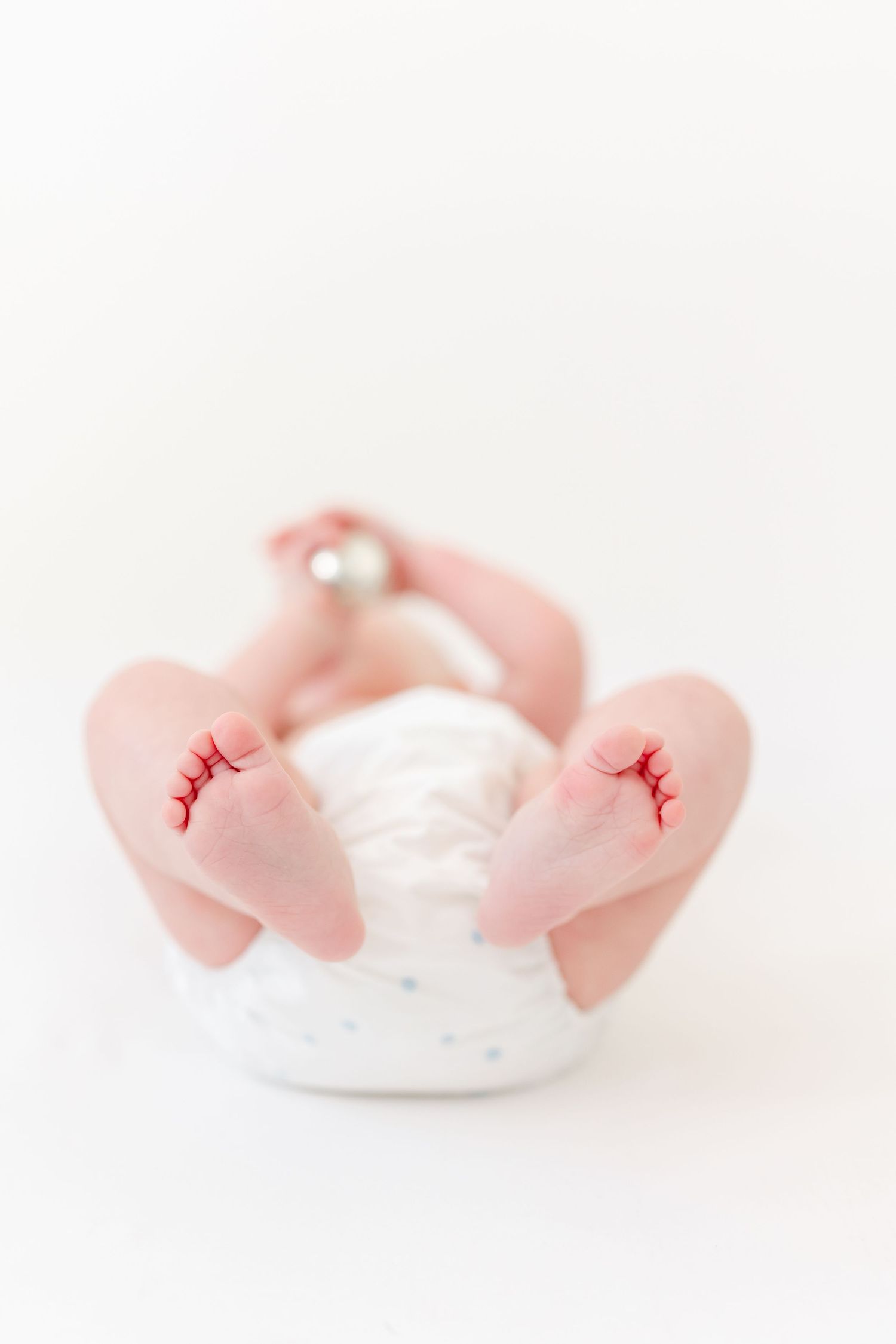 Newborn baby lying on its back in a white diaper, tiny bare feet in focus against a soft white background.