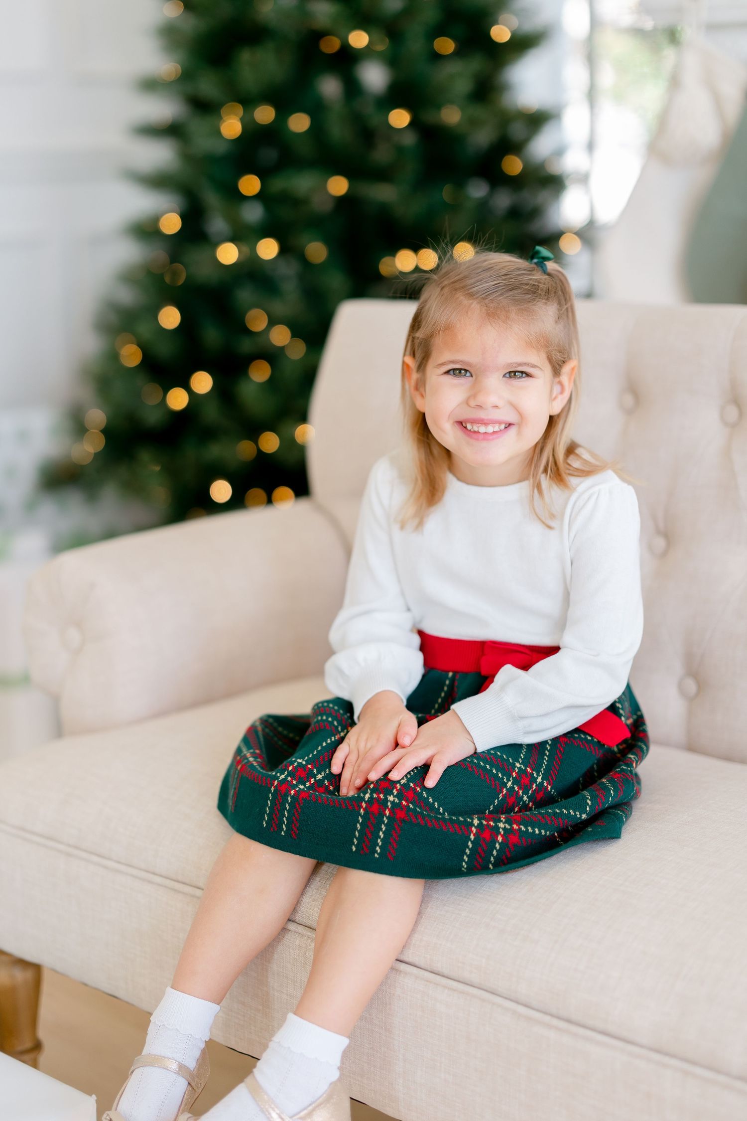 Three holiday photos show a child in festive attire sitting on a white couch with decorated Christmas trees in background.