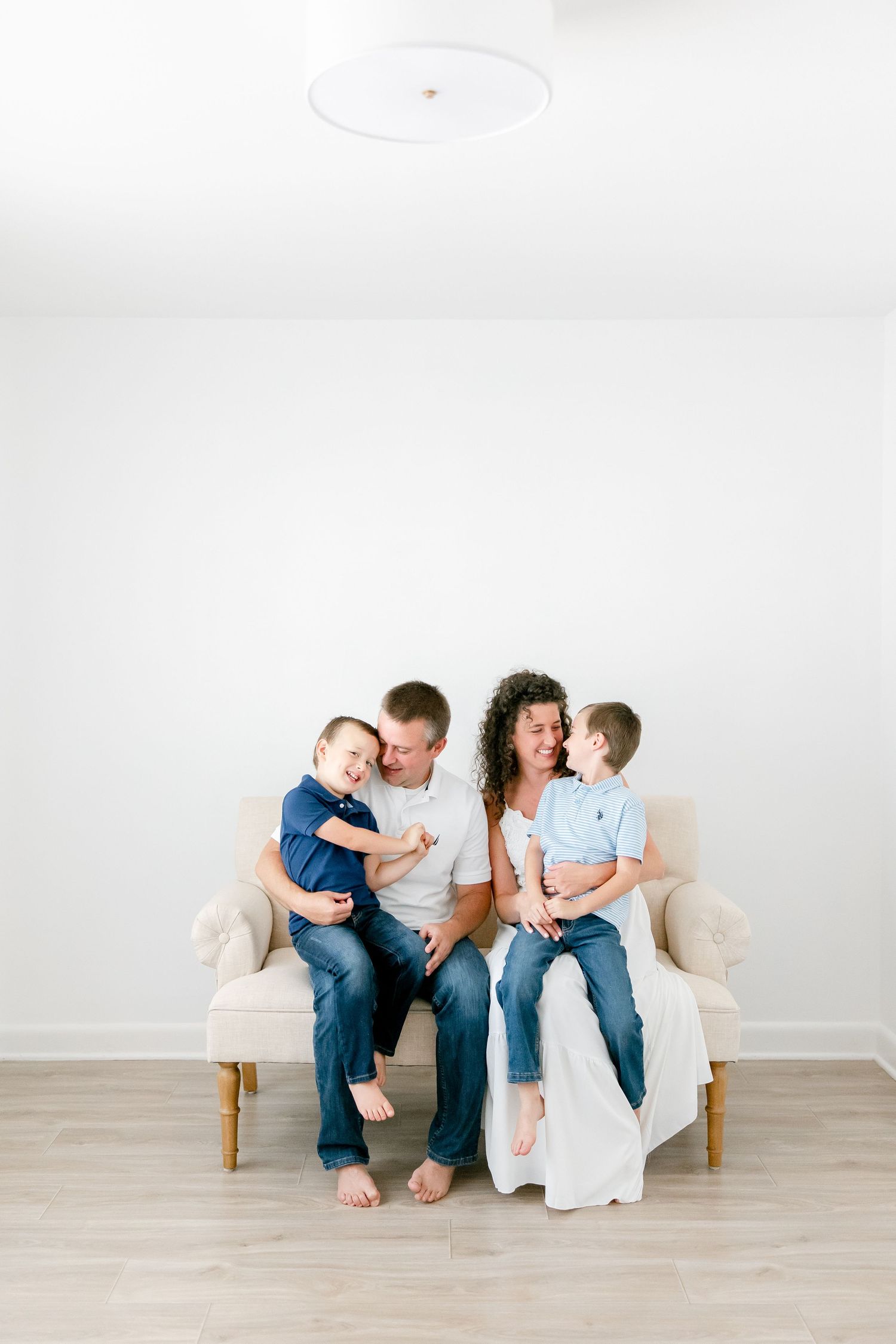 A family shares joyful moments together on a white couch against a minimalist backdrop.