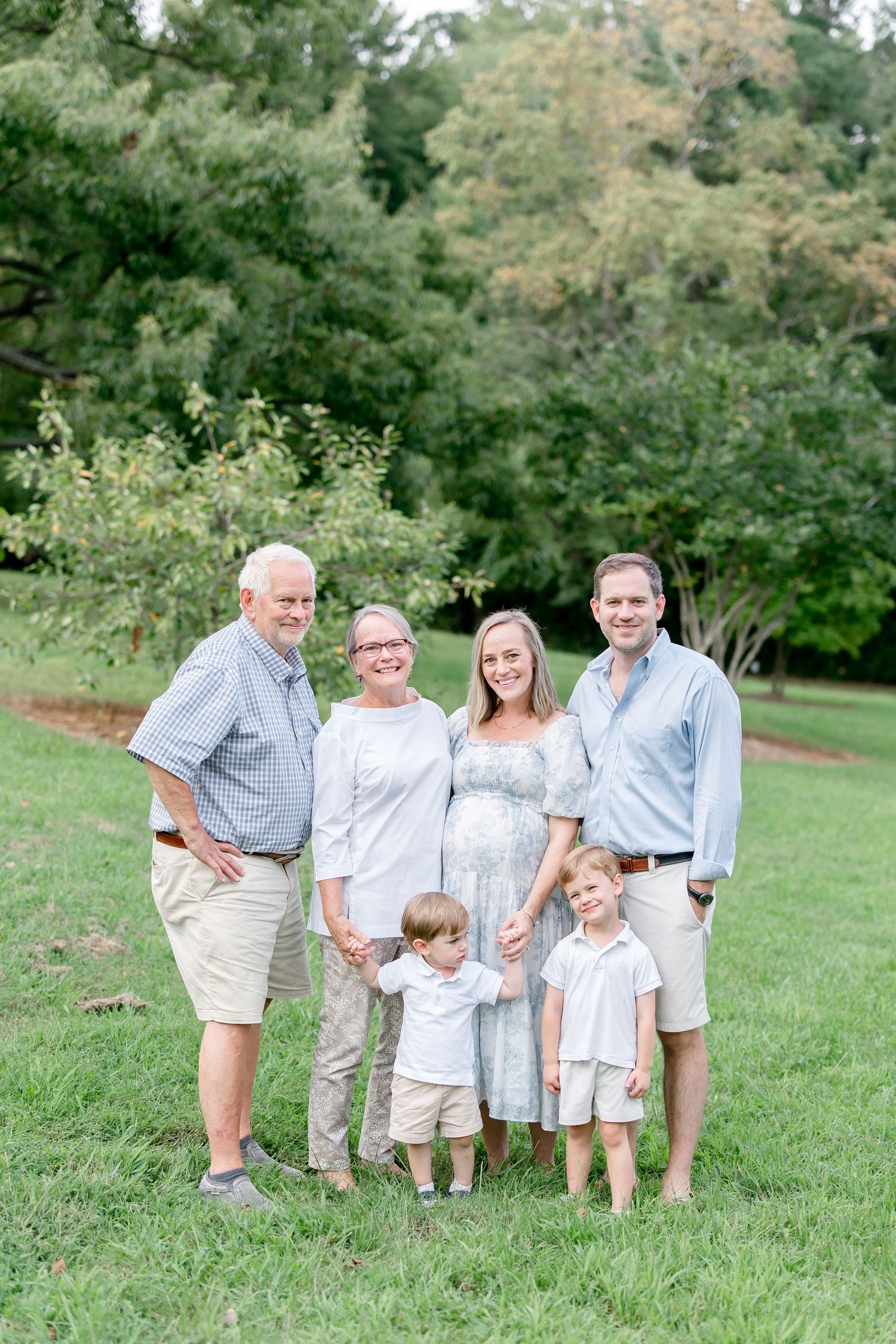 Family group photo on a grassy hill wearing coordinated white and light colored outfits.