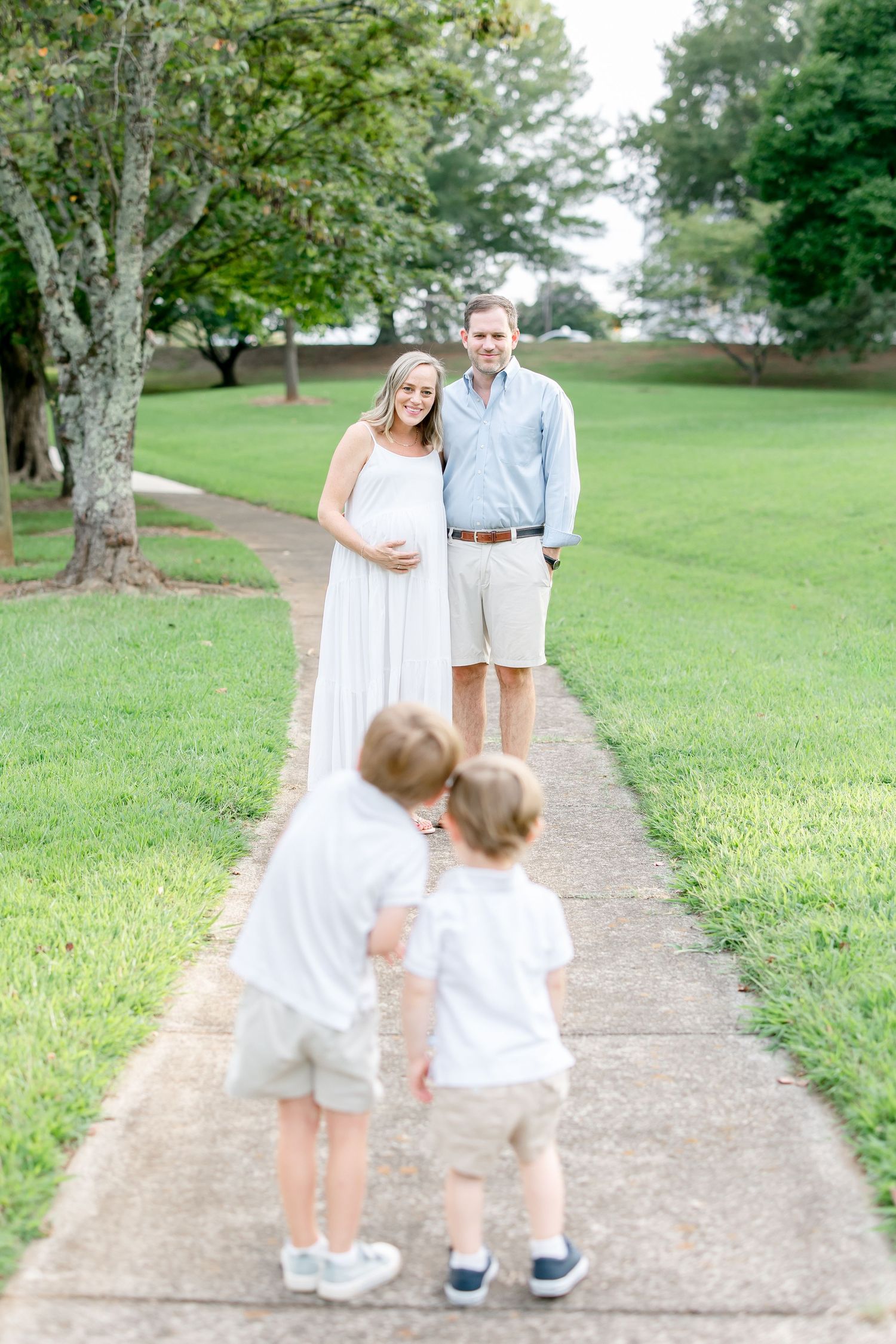 A family enjoying a casual stroll together on a paved path through a green summer park setting.