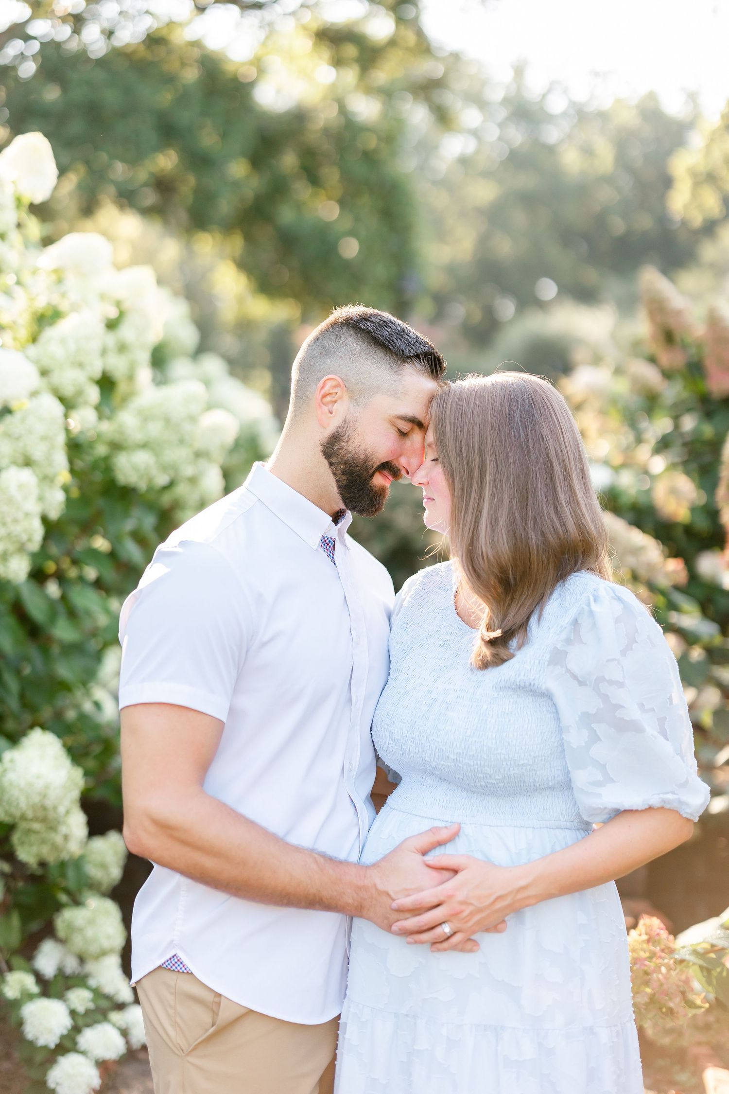 Couple sharing an intimate moment on a terrace with verdant trees and natural sunlight in the background.