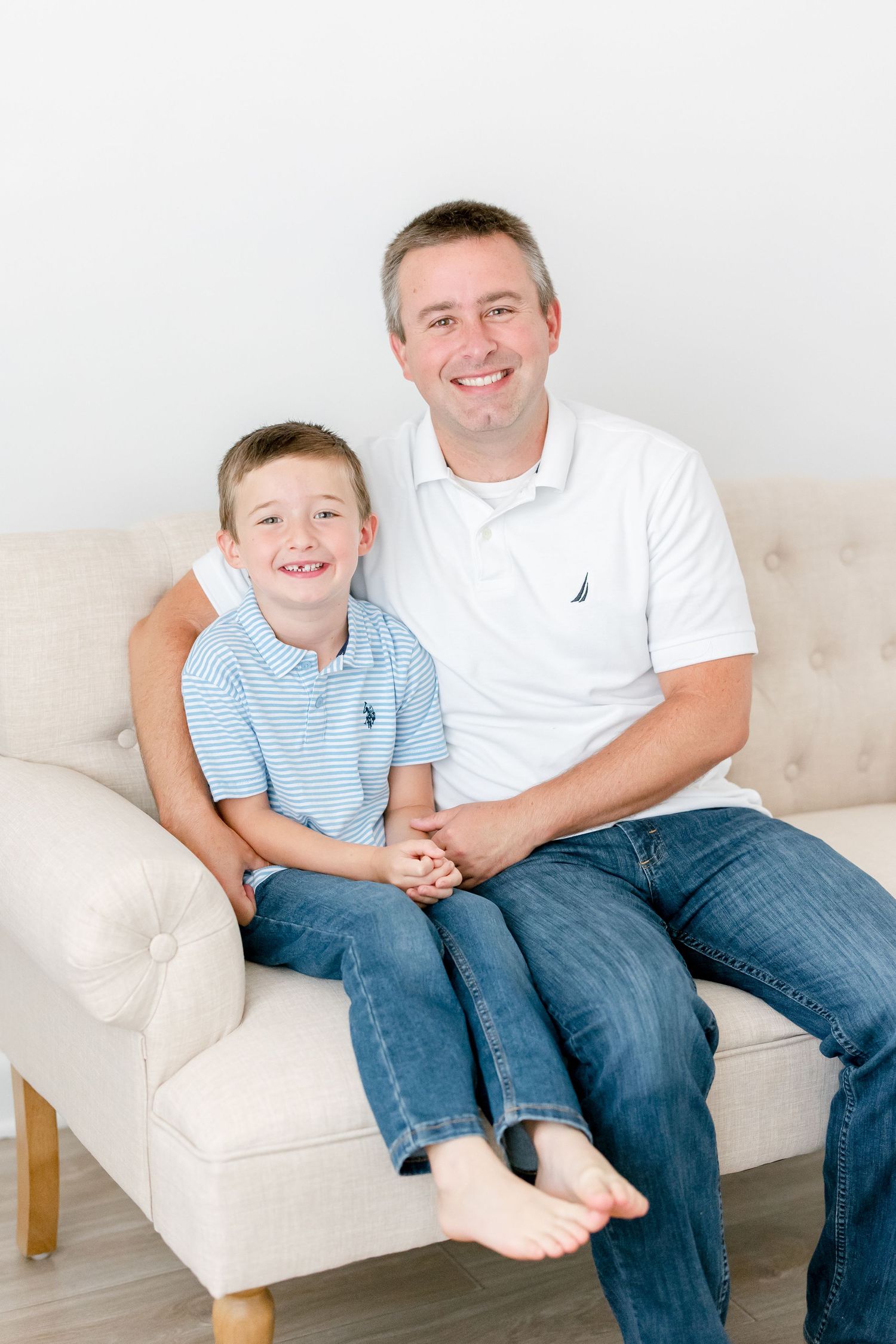 A father and son share a cozy moment of laughter while sitting together on a beige couch.