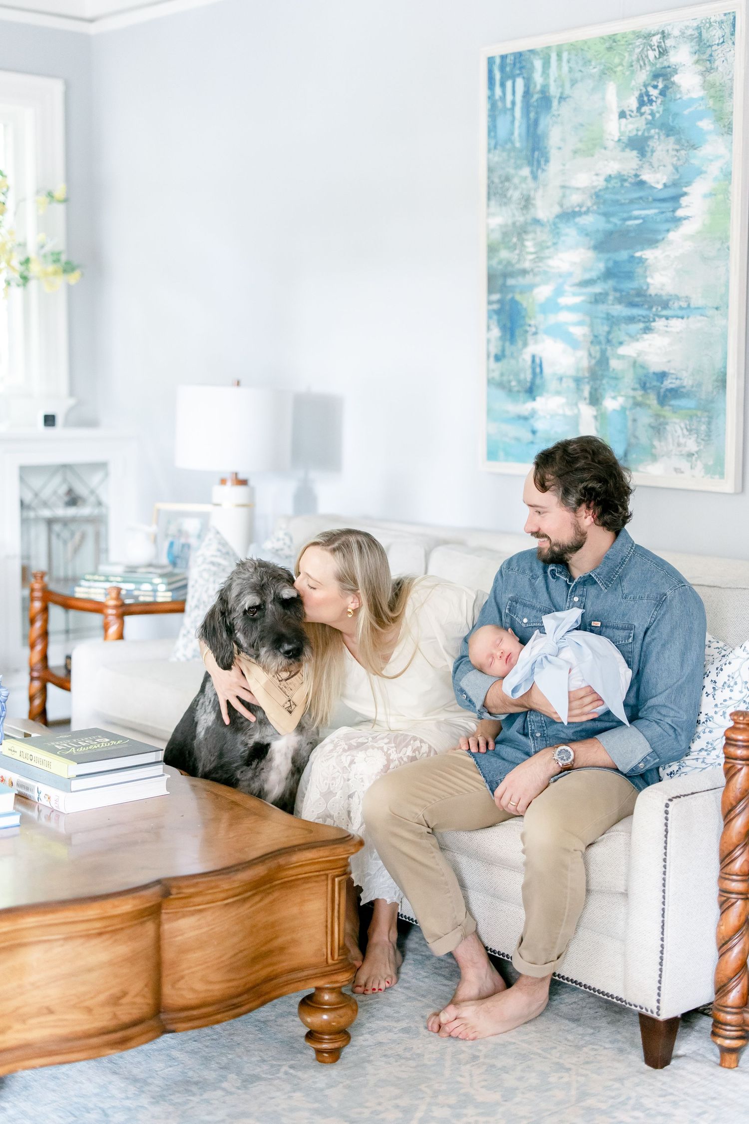 Family relaxing together on white couch with dog and baby in bright modern living room with blue artwork.