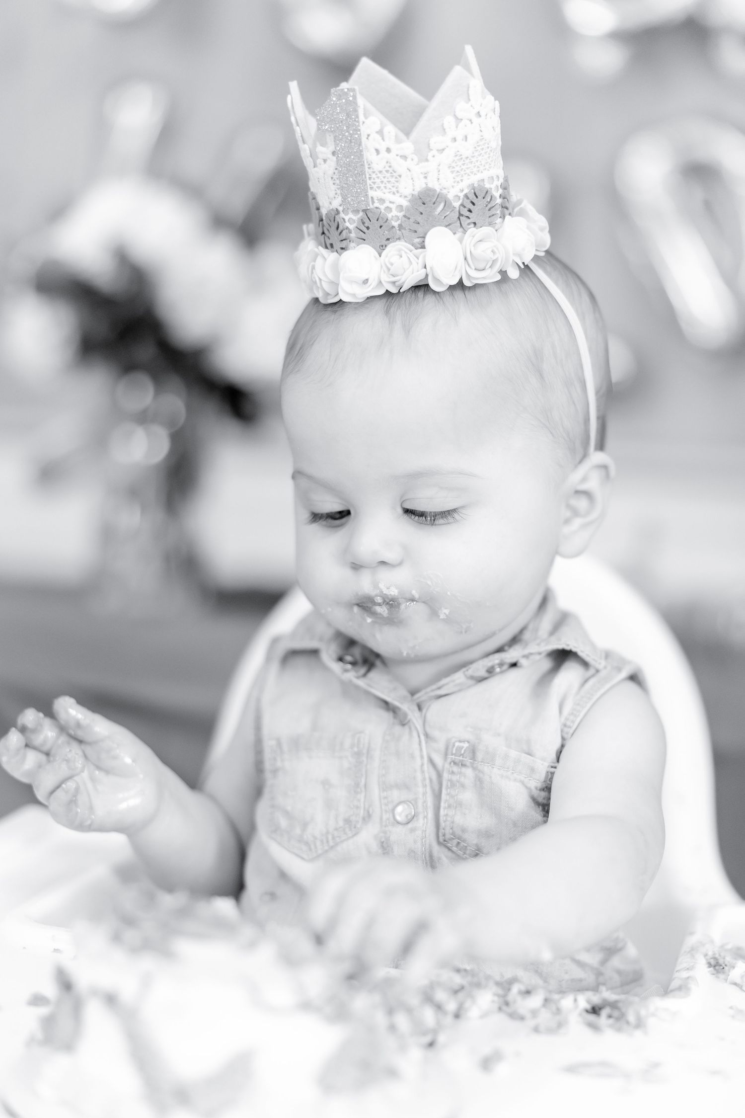 Black and white image of baby in denim wearing lace crown during cake smash.