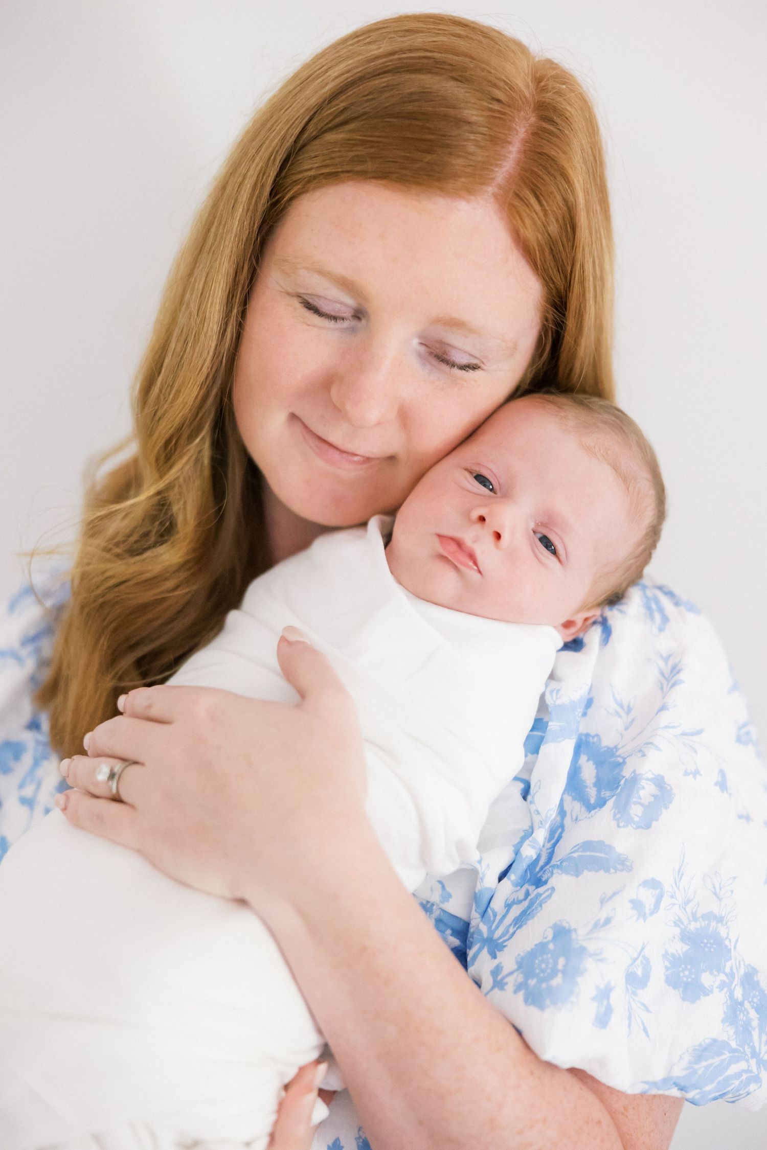 A tender moment between mother and sleeping newborn baby against white background with blue floral accents.