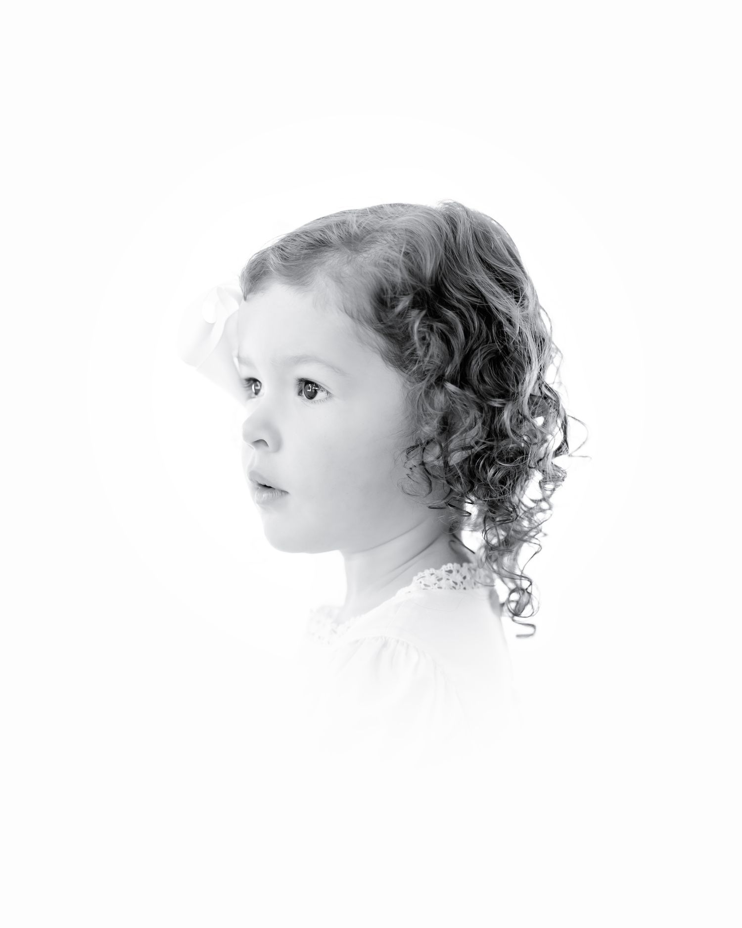 Black and white portrait of a young child with curly hair looking off to the side in a soft ethereal style.