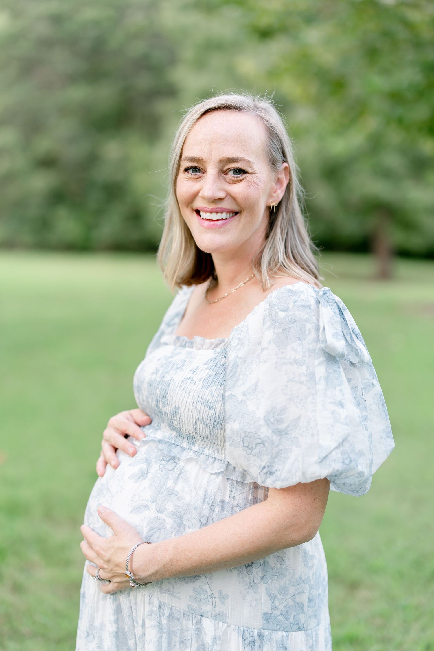 Maternity photos showing a woman in a delicate blue dress smiling in a park setting.