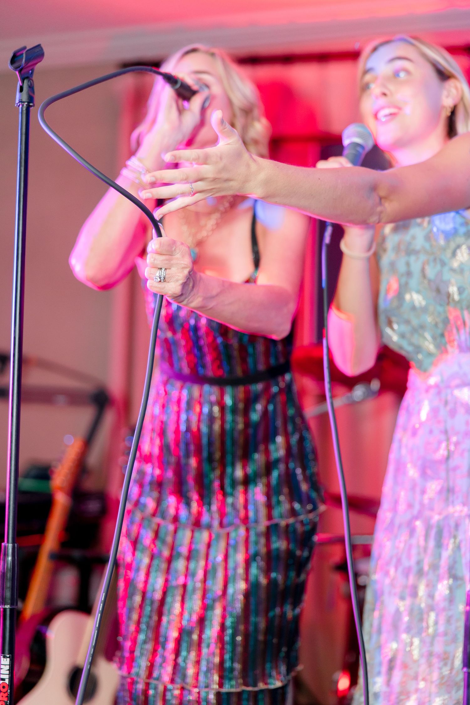 Performers singing enthusiastically at a karaoke show with pink and blue stage lighting.