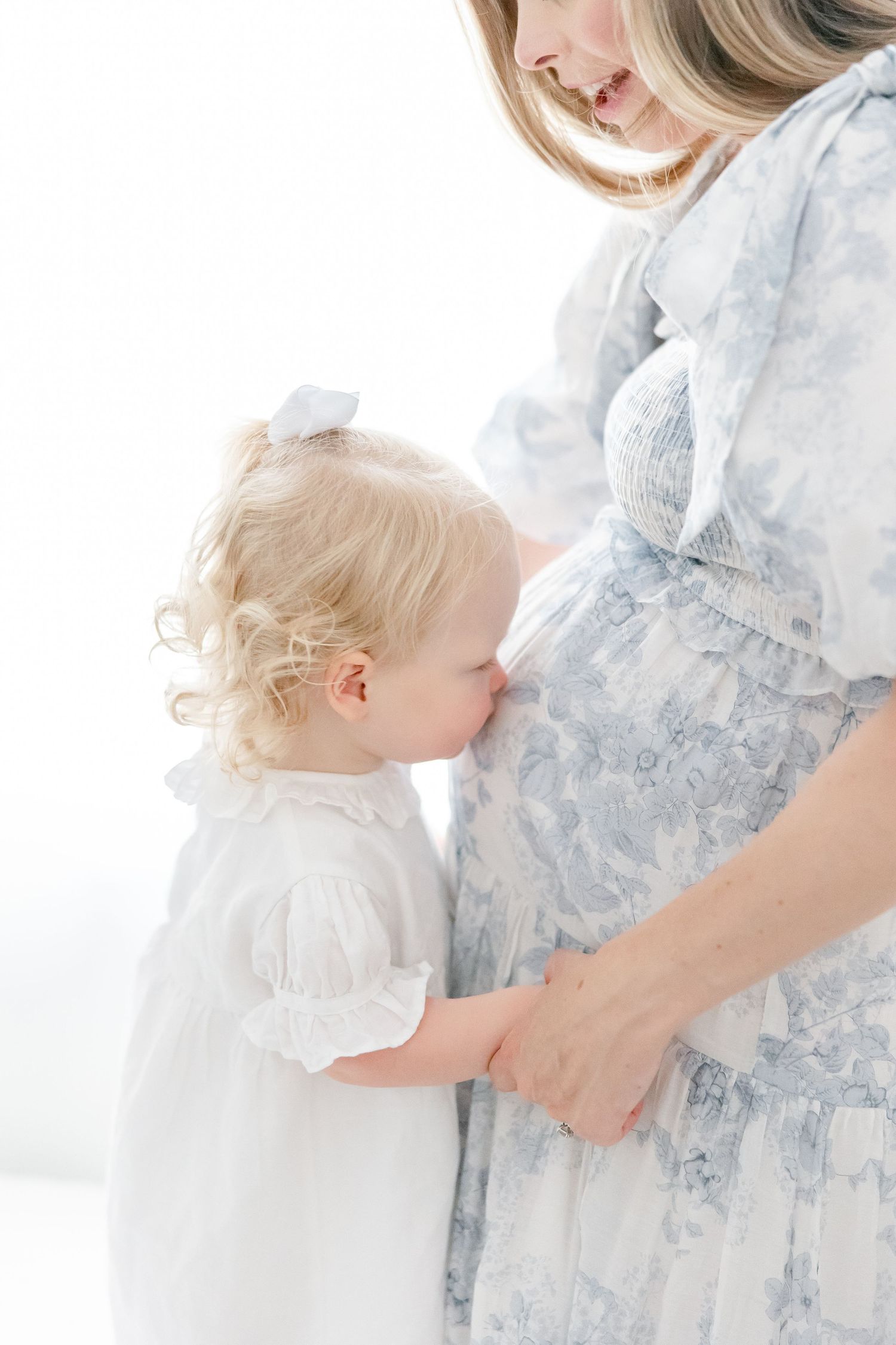 An intimate maternity photo showing a close embrace between parent and child in soft white lighting.