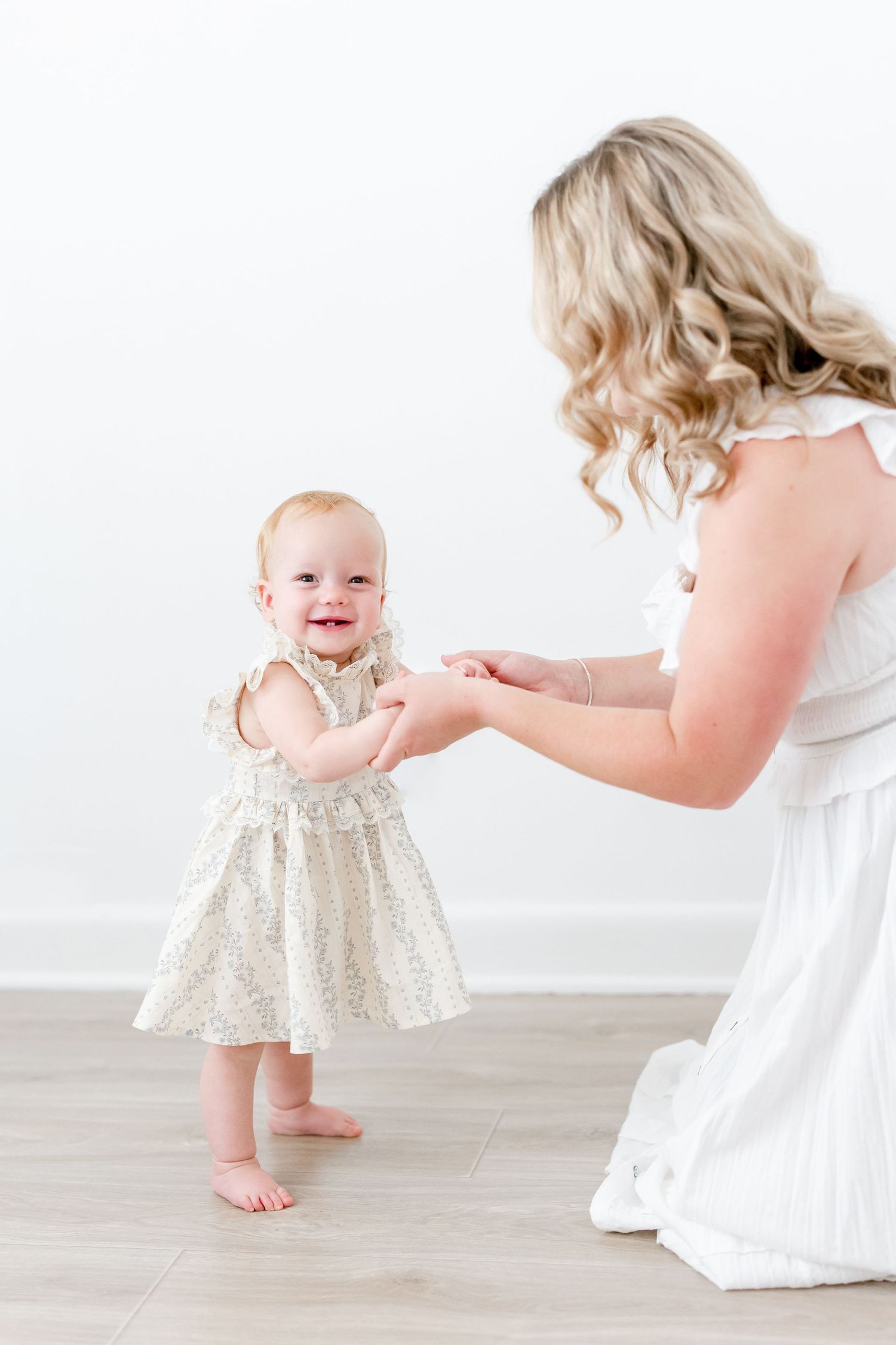 A series of photos showing a baby in a sparkly dress walking towards someone in a white dress on a white background.