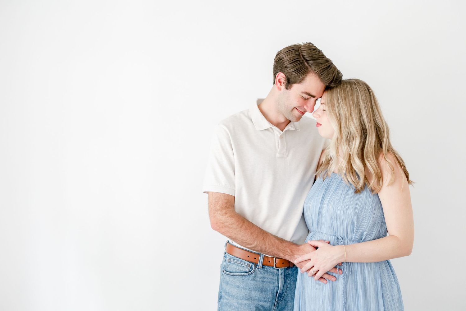 A couple in white and blue outfits embrace tenderly against a light background.