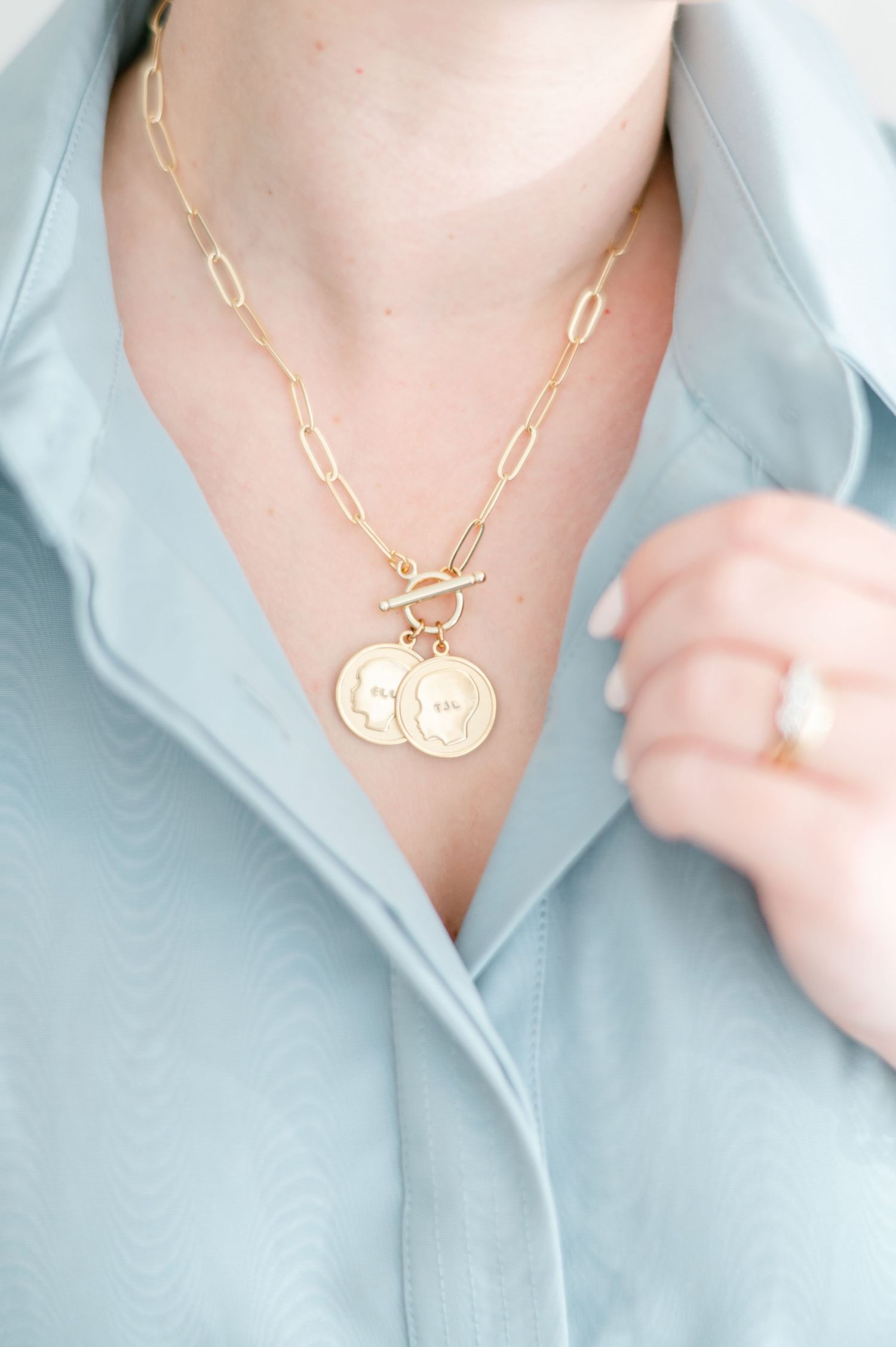 Gold chain toggle necklace with coin pendants worn with light blue button-up shirt.