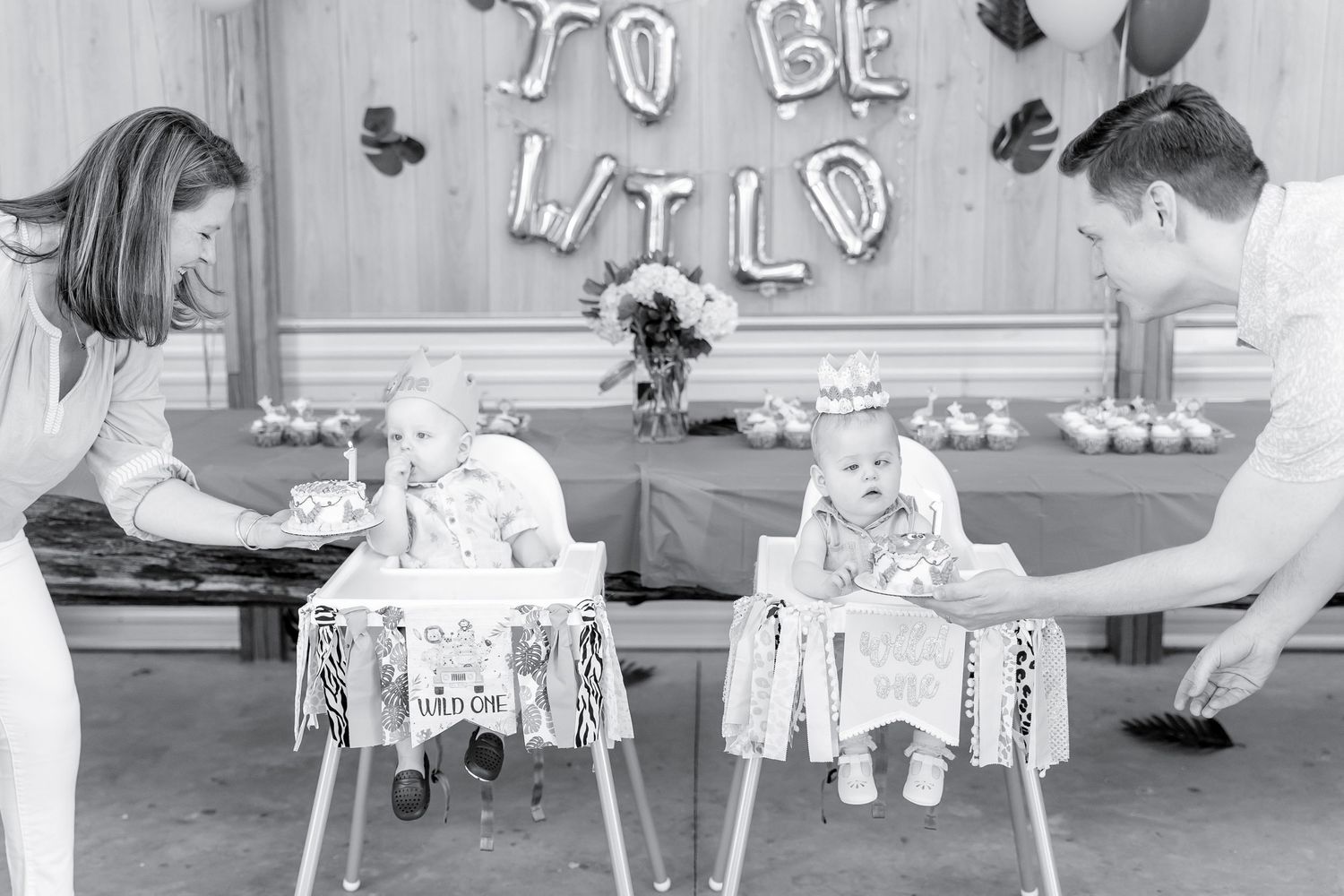 Black and white photo of family celebrating with twin babies in decorated highchairs.