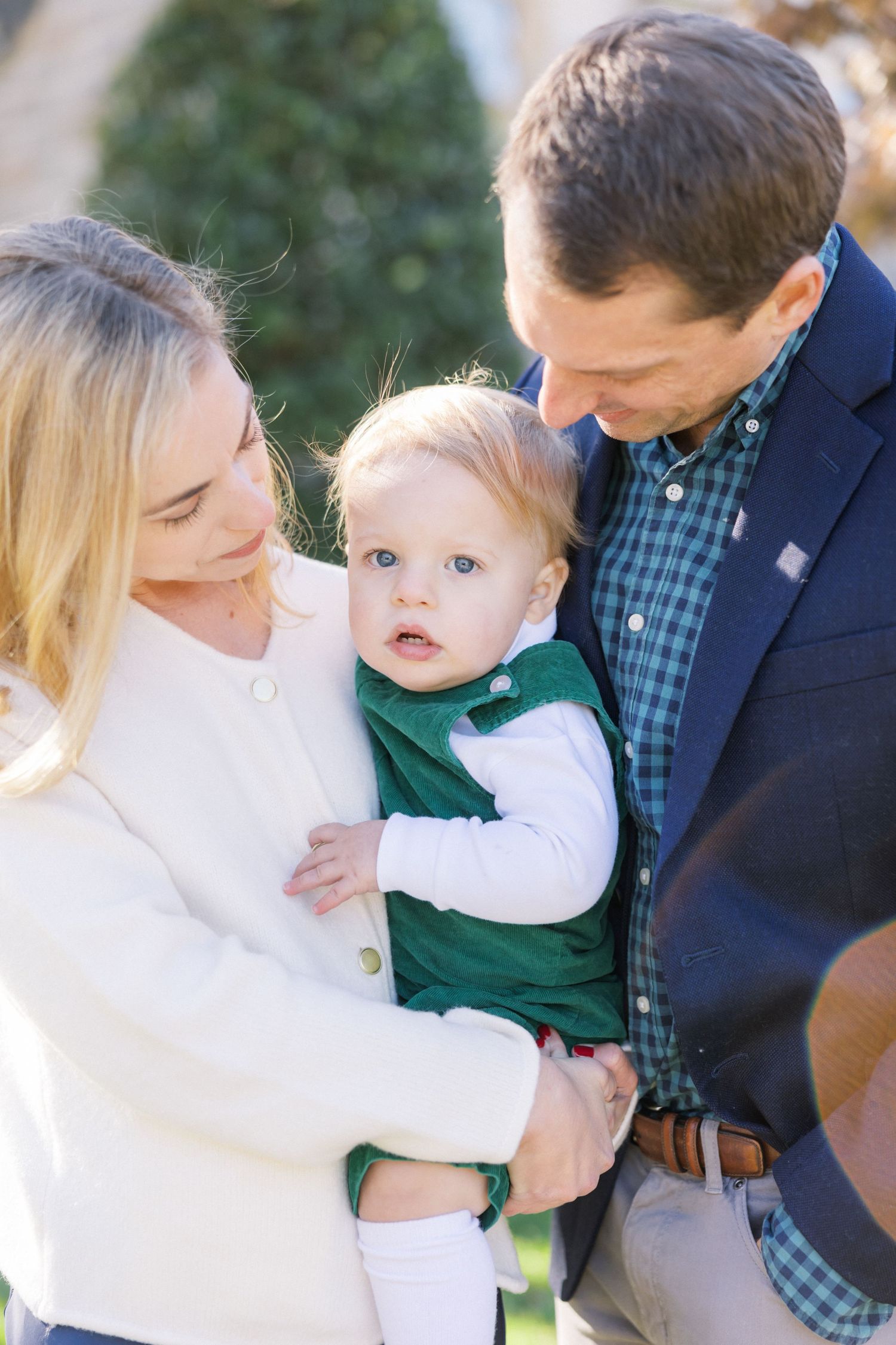 A young family dressed in blue and white shares an intimate outdoor moment together in natural sunlight.