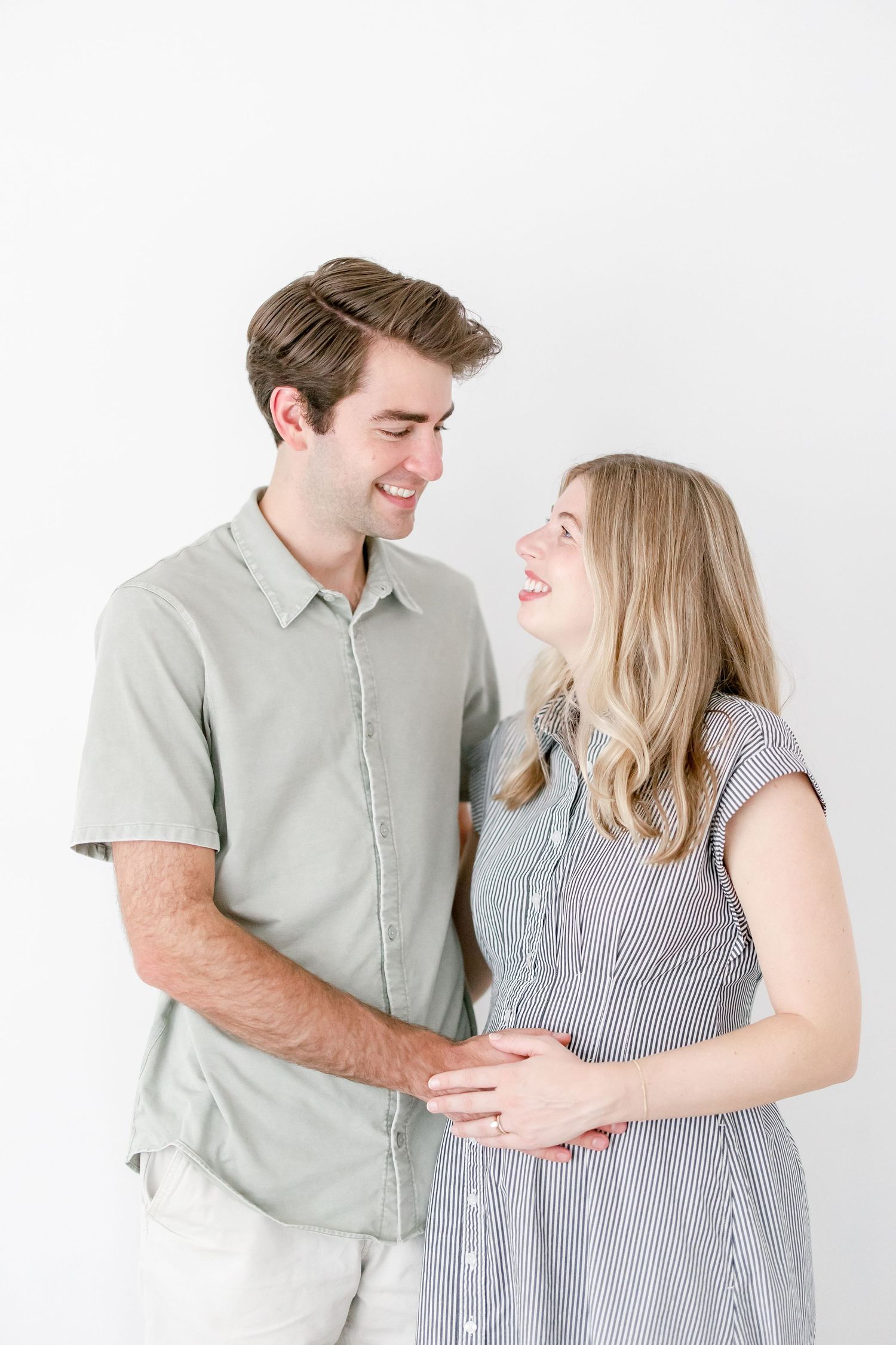 Intimate maternity portraits of expecting couple in casual attire against white background.
