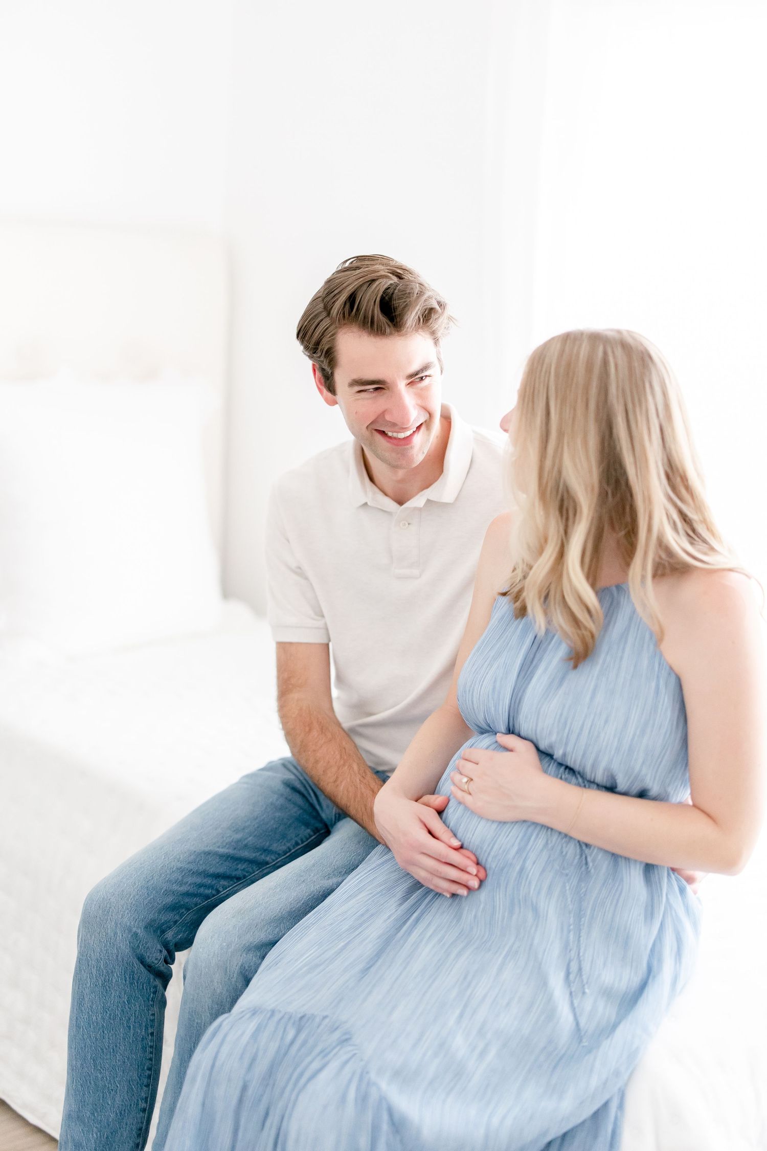 Couple in casual clothing sit together on white bench sharing intimate moment in bright studio setting.