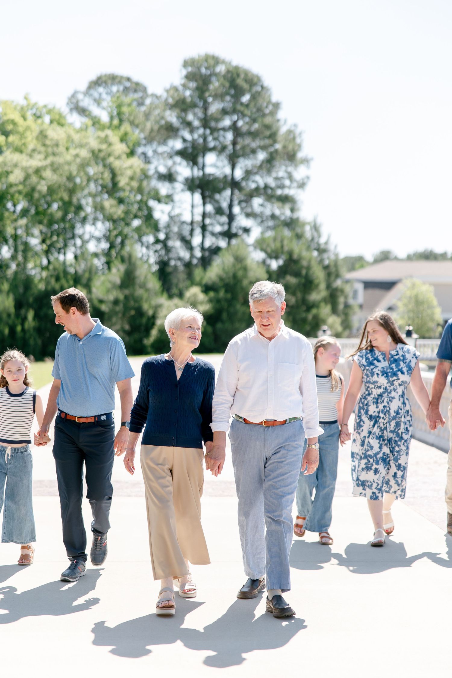 A group of people strolling together on a sunny path with tall pine trees in the background.