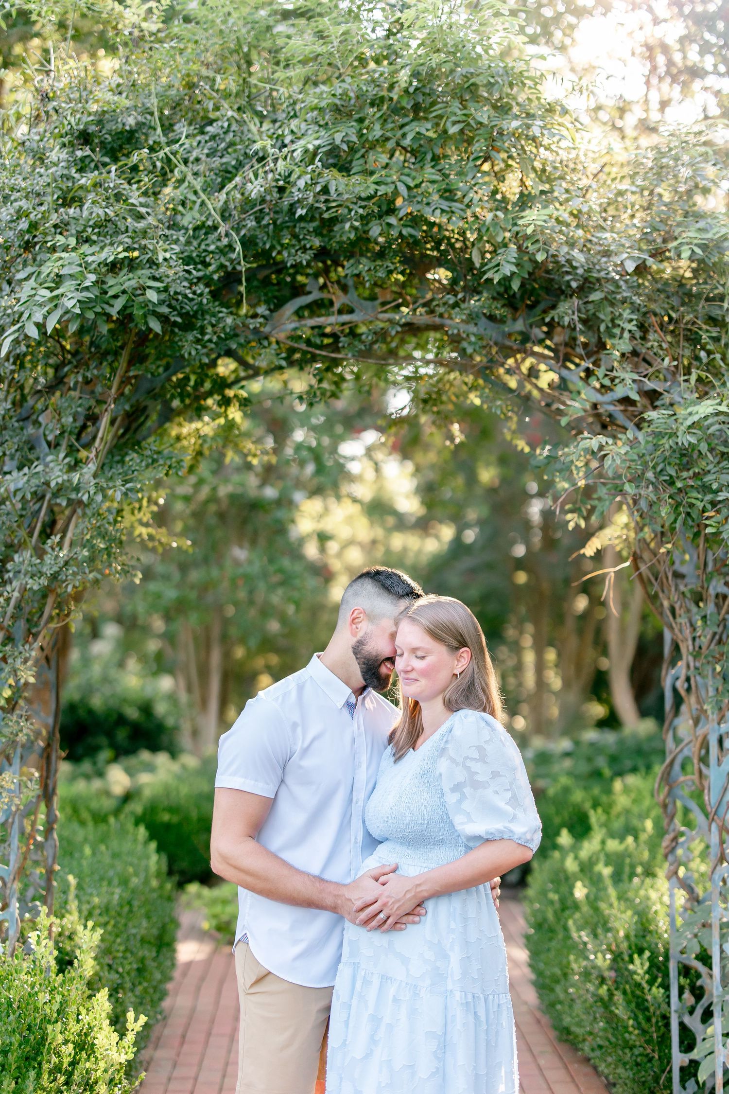 Romantic outdoor maternity photoshoot with couple posing in front of lush greenery.