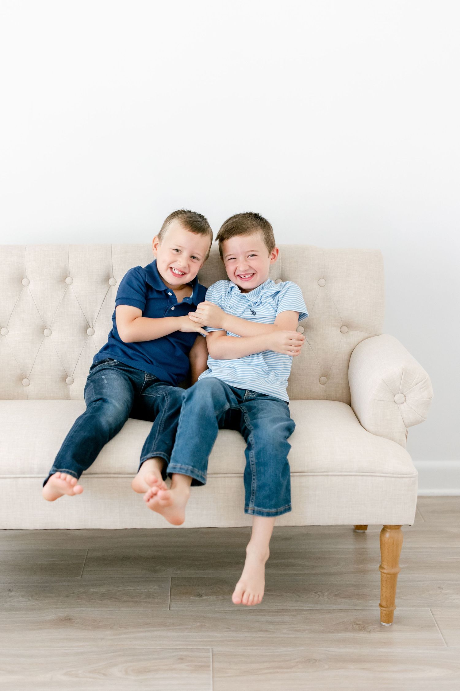 Kids in casual clothes having fun and giggling while sitting on a beige tufted sofa.