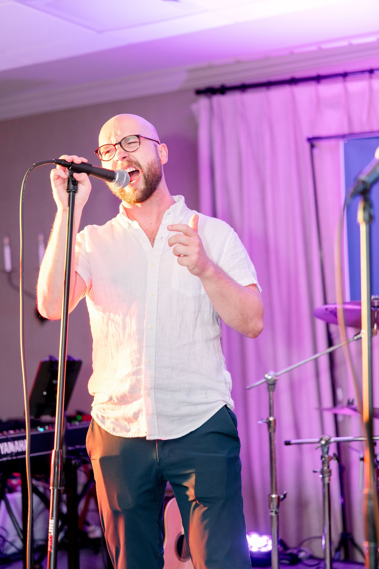 A performer in white singing passionately on stage with purple lighting effects in the background.