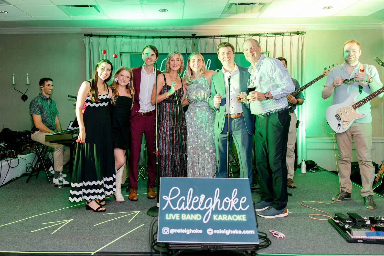 Group photo of the Raleighoke live band and karaoke performers on stage with their logo sign.