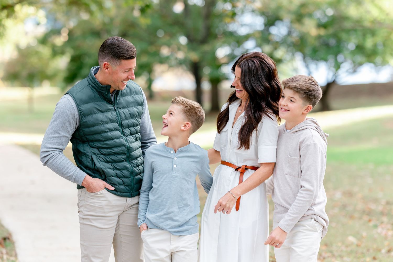 A happy family of four laughing together outdoors, with two boys and their parents dressed in casual, coordinated outfits.