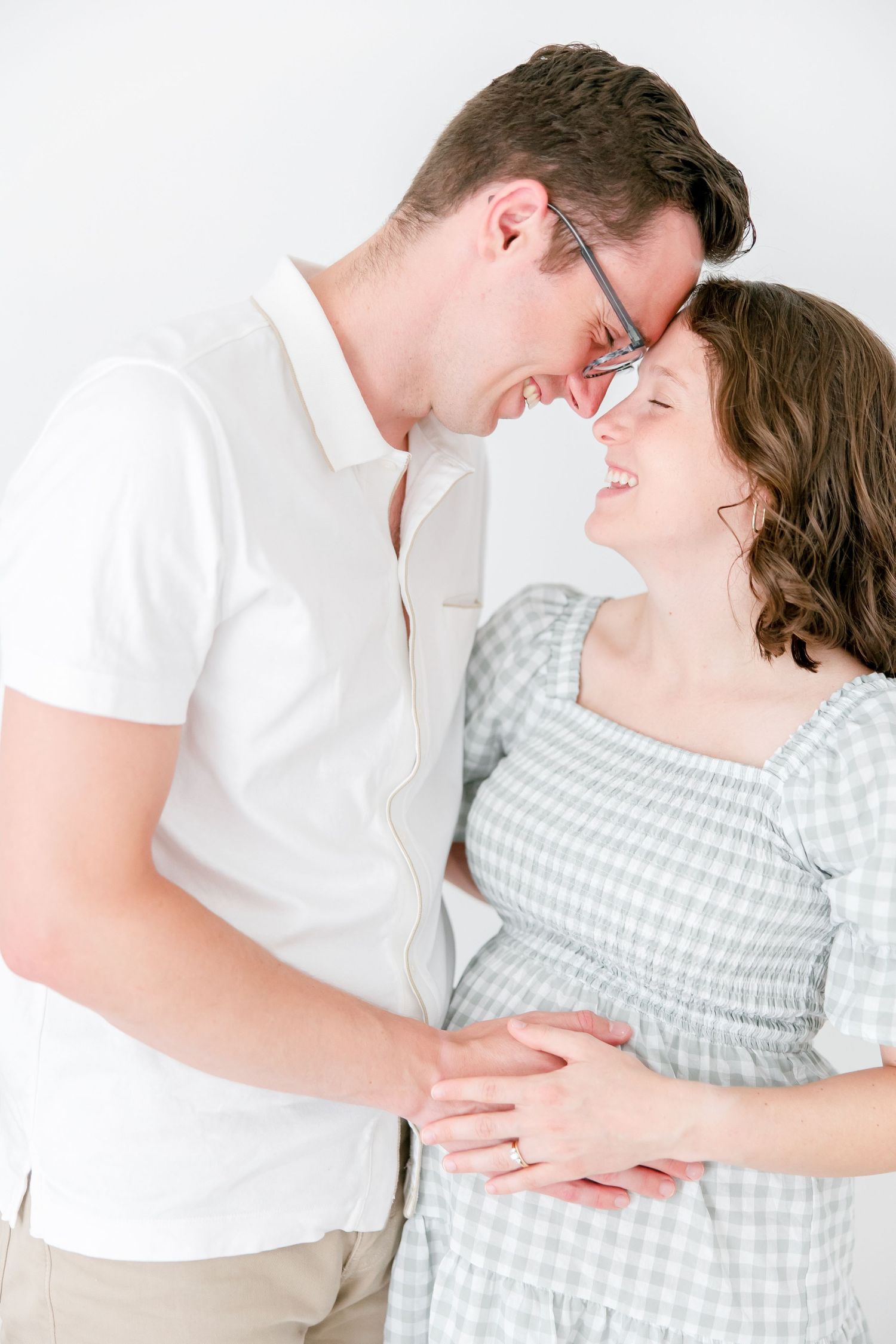 A romantic maternity portrait shows a couple in white and gingham sharing an intimate moment.
