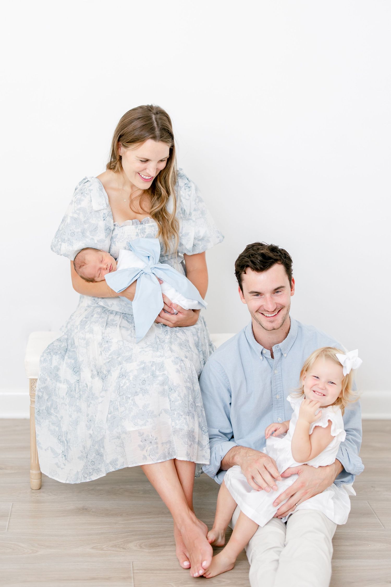 Family in coordinating blue and white outfits pose together on light wood floor in candid lifestyle portraits.