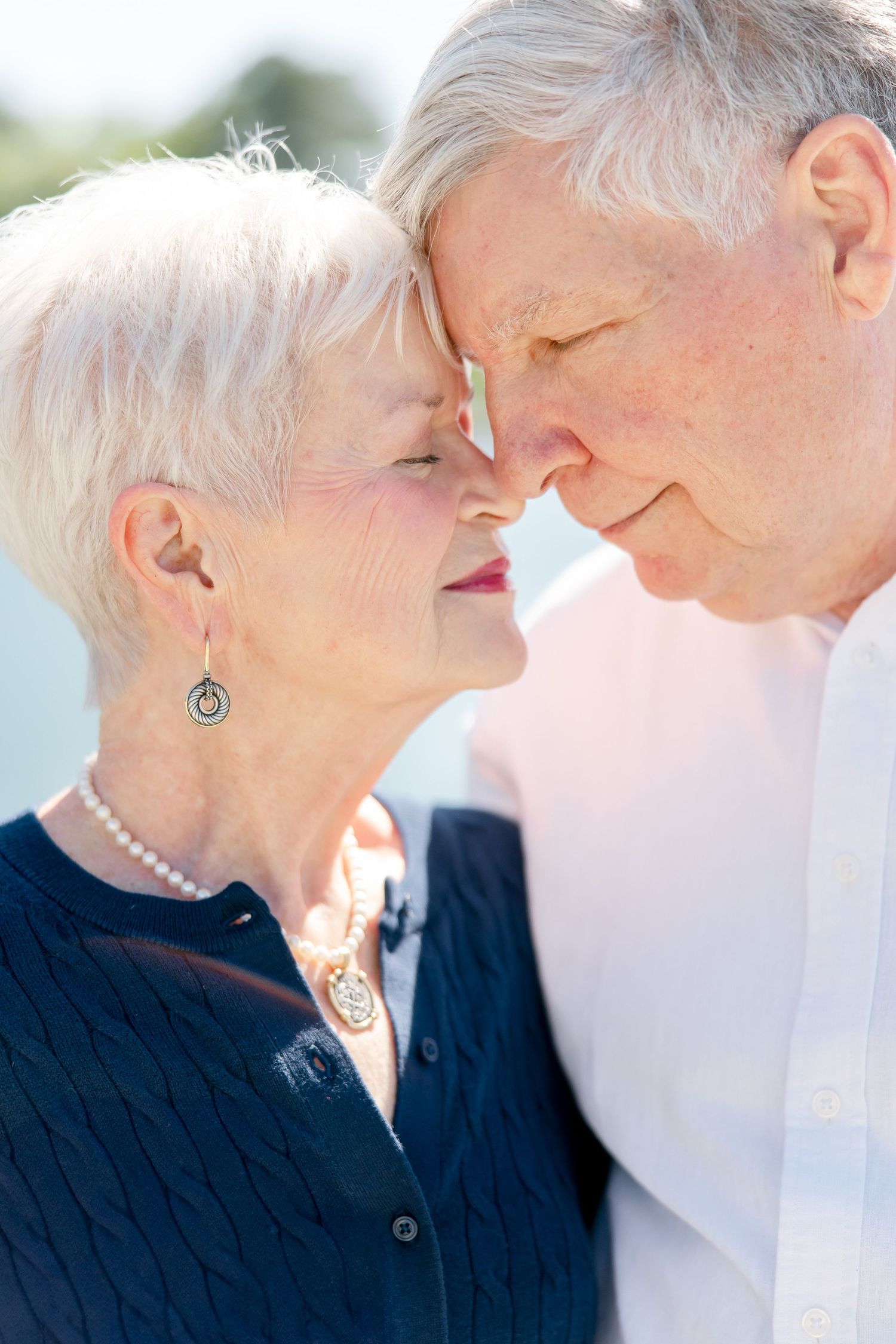 Loving elderly couple in white and navy clothing share tender moment outdoors.