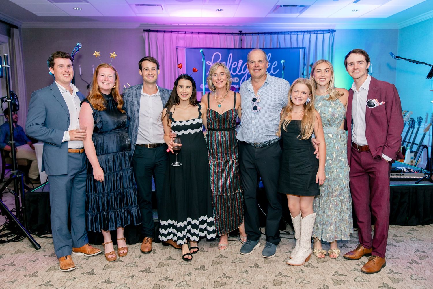 Group of wedding party guests posing in a line against a blue-lit backdrop at an indoor venue.