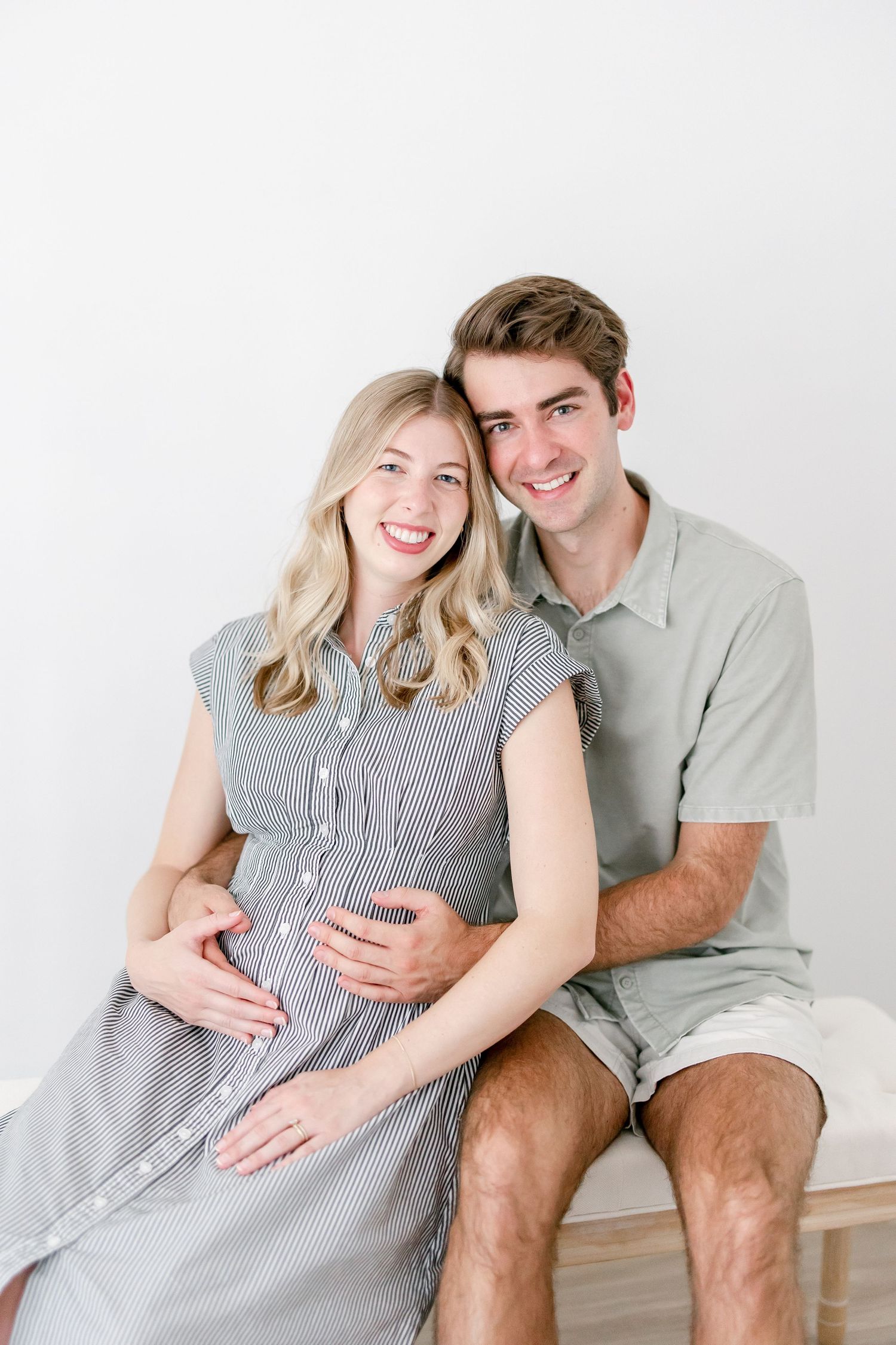 Couple sharing joyful moments during maternity photo session in white studio.