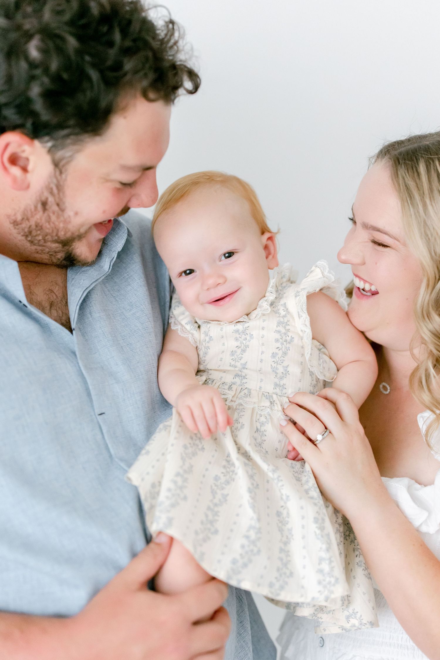 A family of three shares intimate moments in a bright white studio setting wearing light colored clothing.