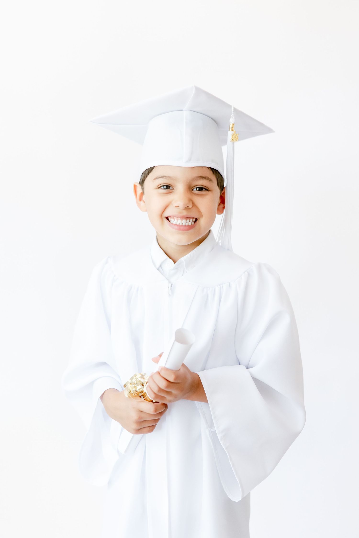 Young child in white chef uniform and hat smiling while holding cooking utensils in professional kitchen setting.