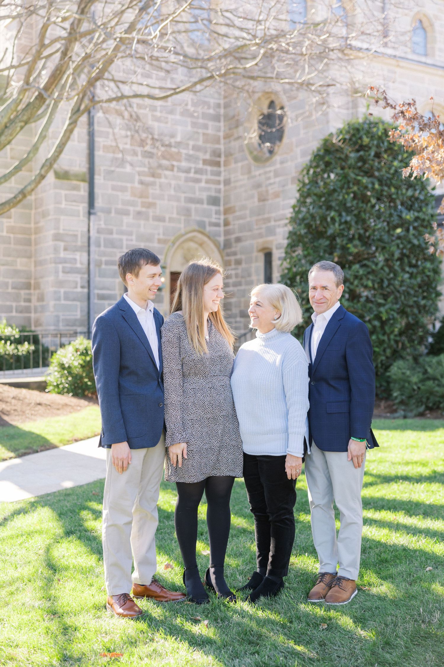 A family dressed in business casual attire poses together outside a stone church building on a sunny day.