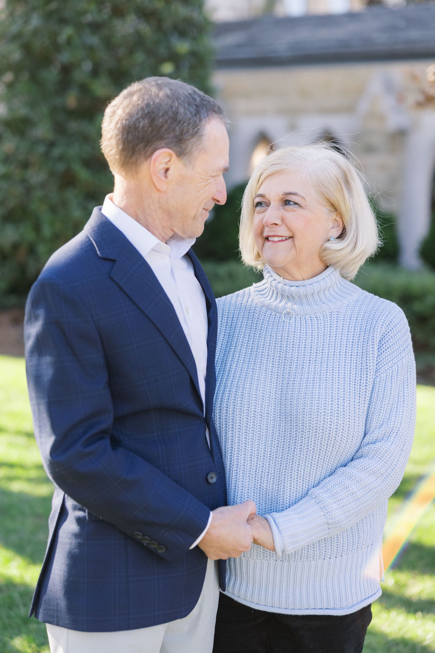 Senior couple sharing a loving moment outdoors, wearing a navy blazer and light sweater on a sunny day.