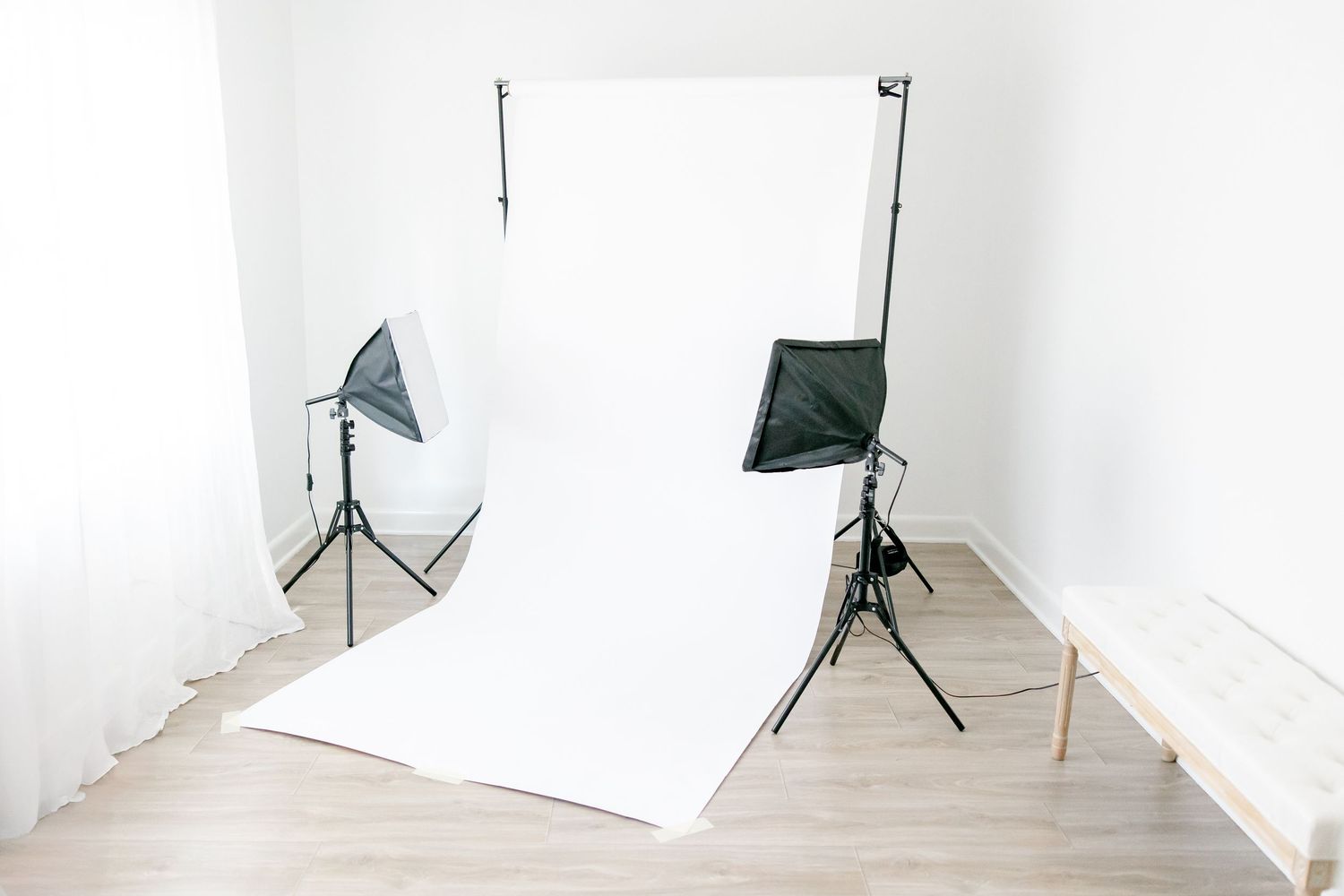 Professional photography studio setup with white backdrop and two softbox lights on tripod stands in bright room.