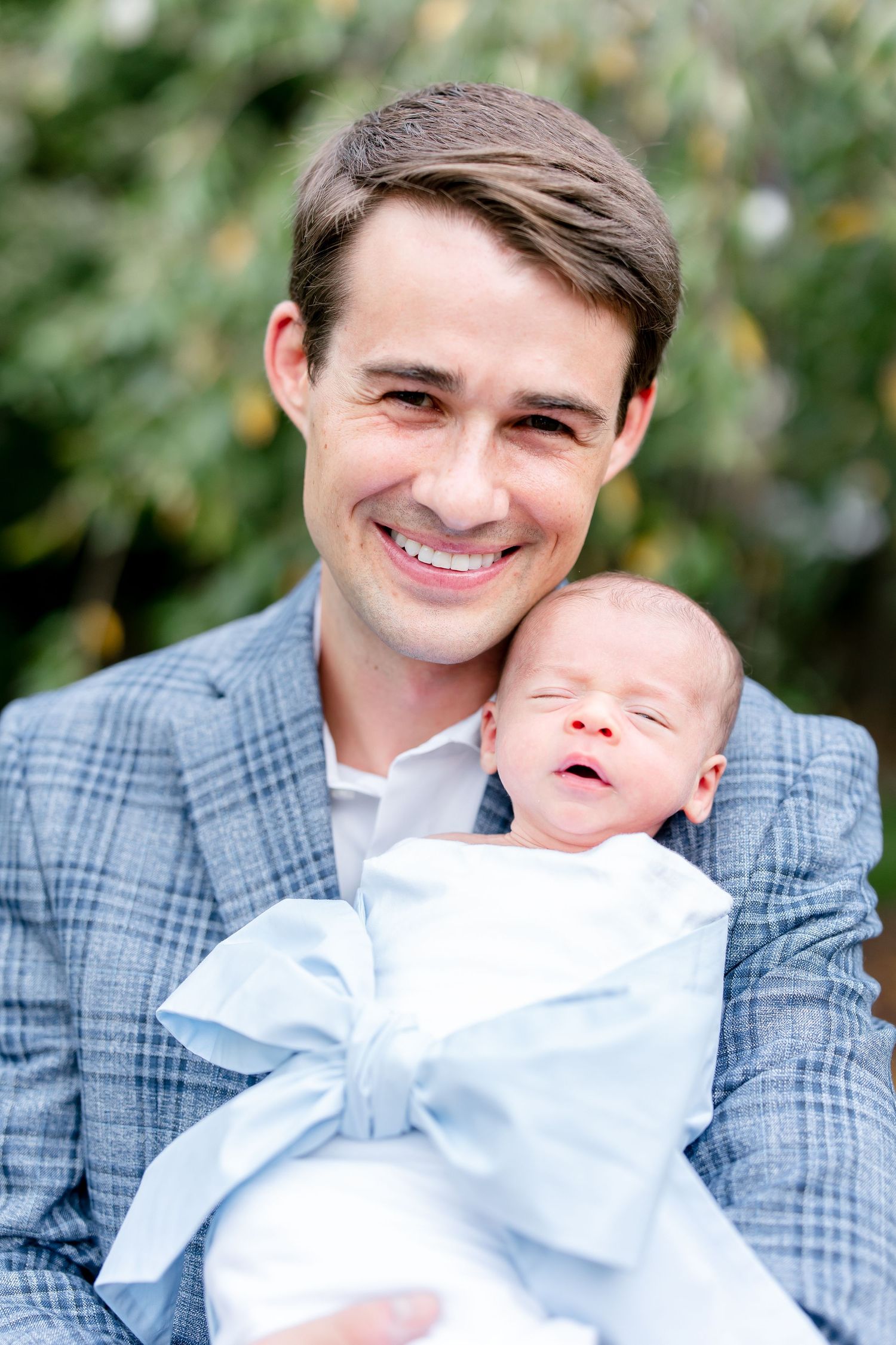 Sweet candid moments between father and newborn baby in outdoor setting.