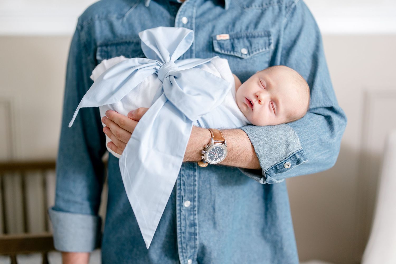Four images show someone holding a baby wearing a light blue bow while standing in a softly lit indoor setting.