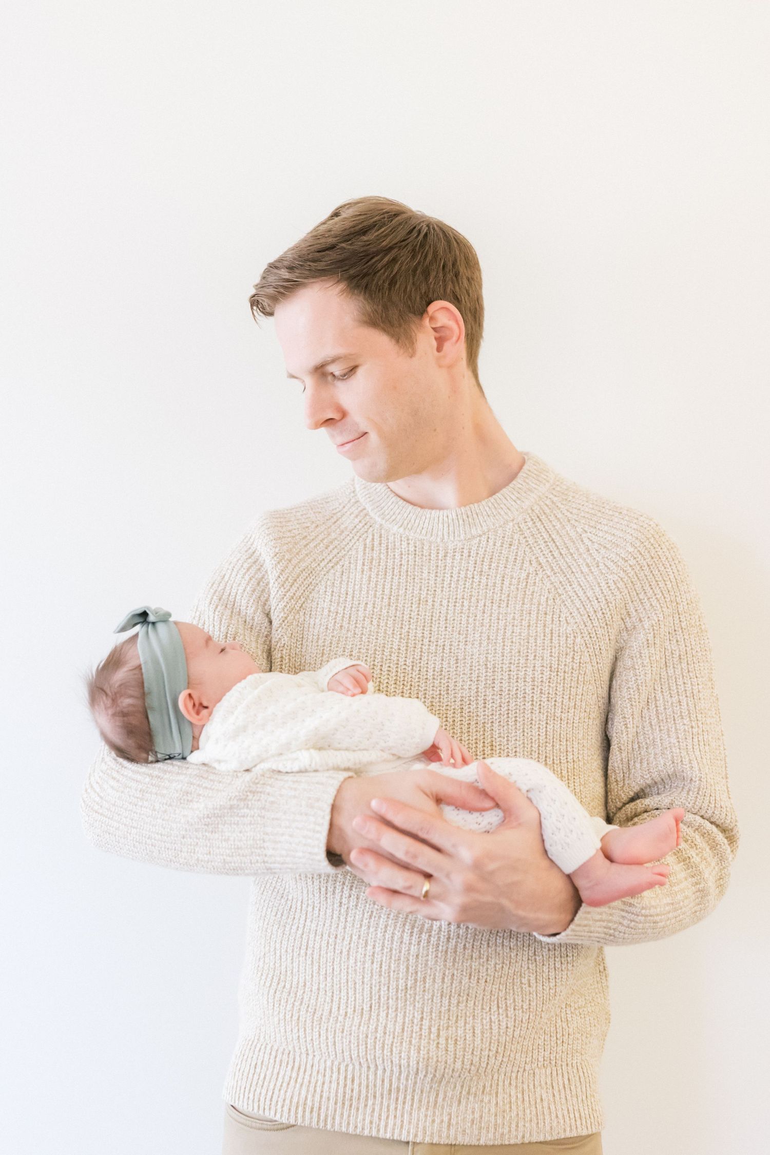 Parent in beige sweater holding swaddled newborn baby against white background in three gentle poses.