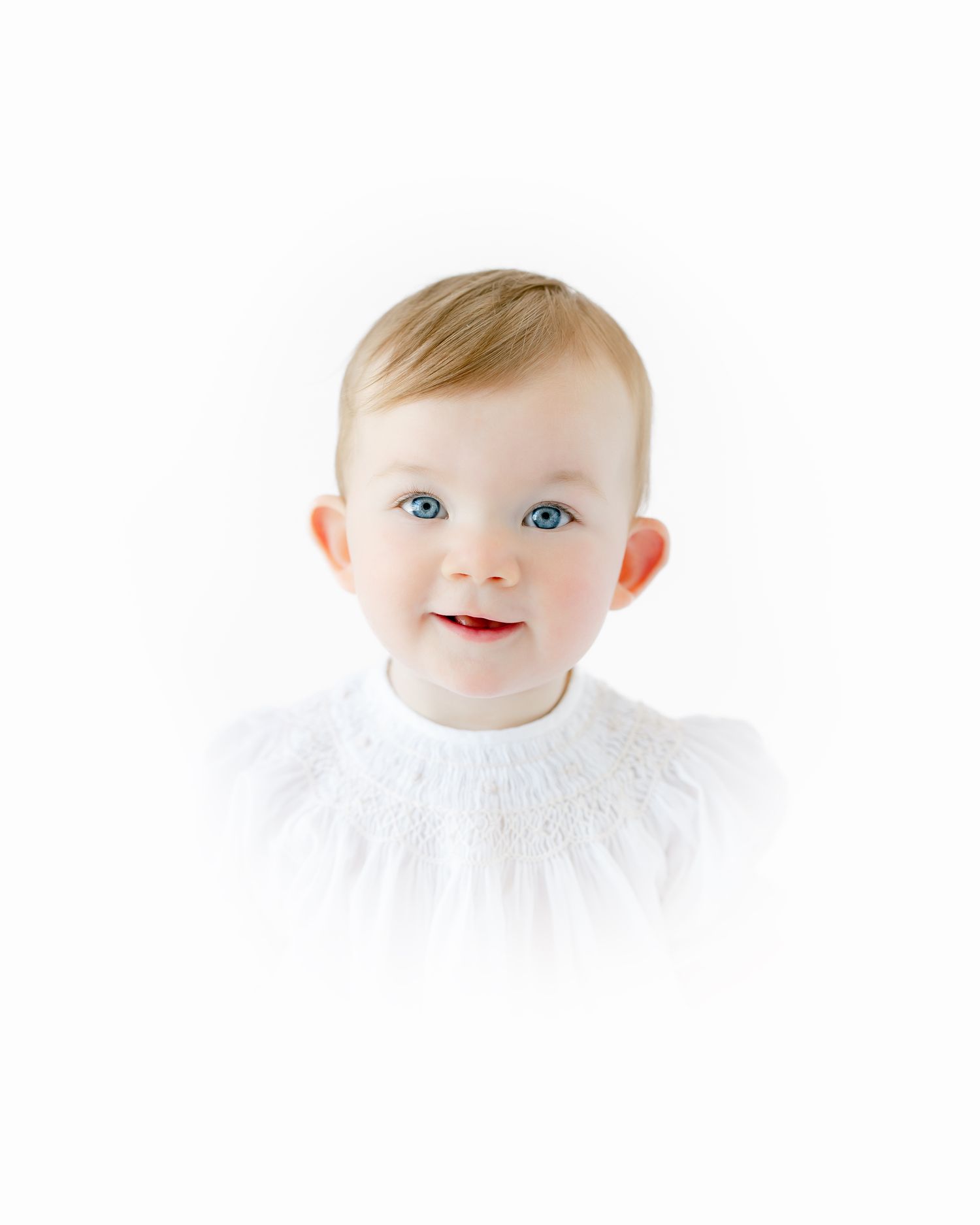 Adorable baby with blue eyes smiling, wearing a white knit top, against a clean white background.