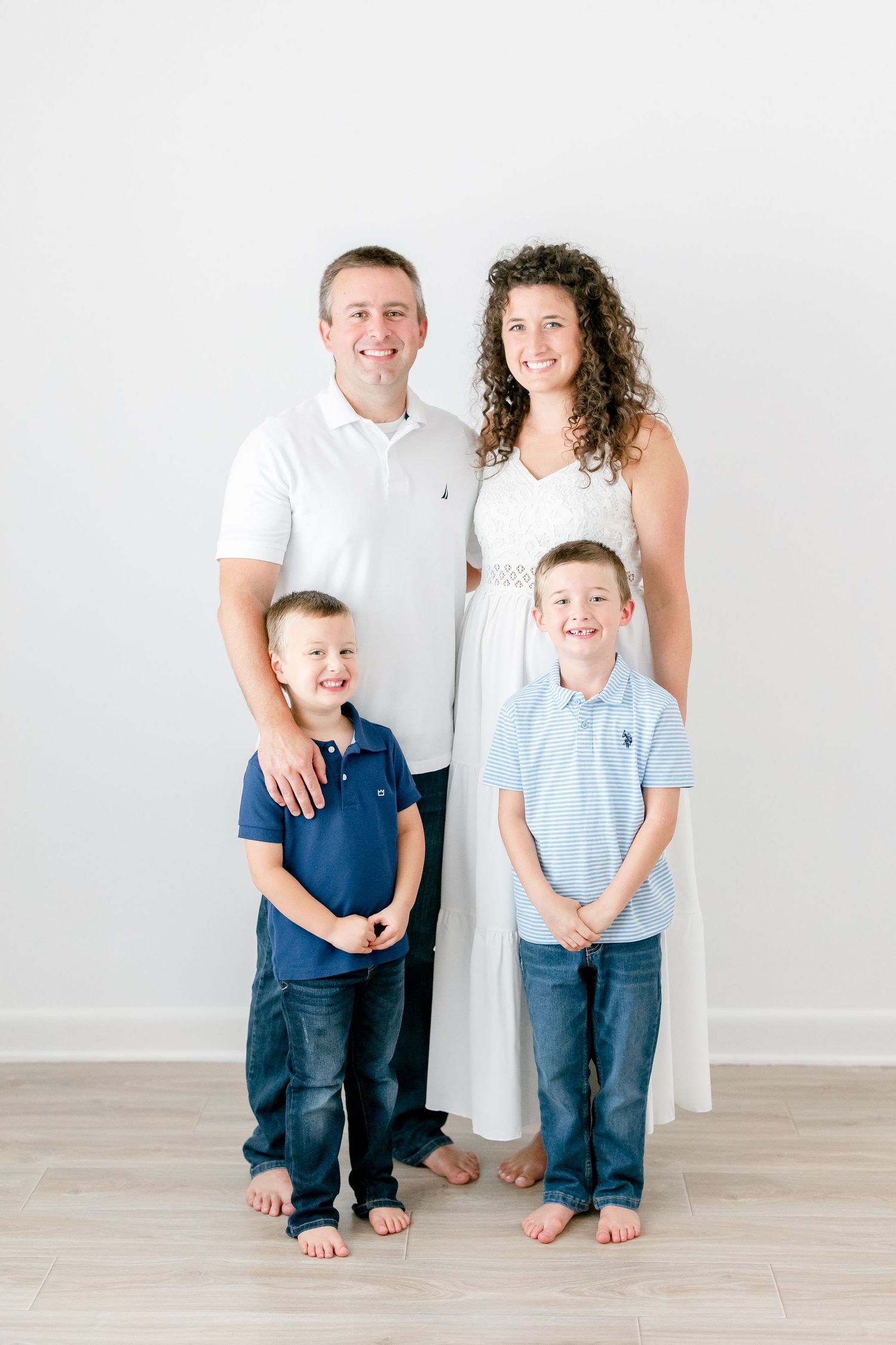 Family wearing coordinated blue and white outfits poses together against white background.