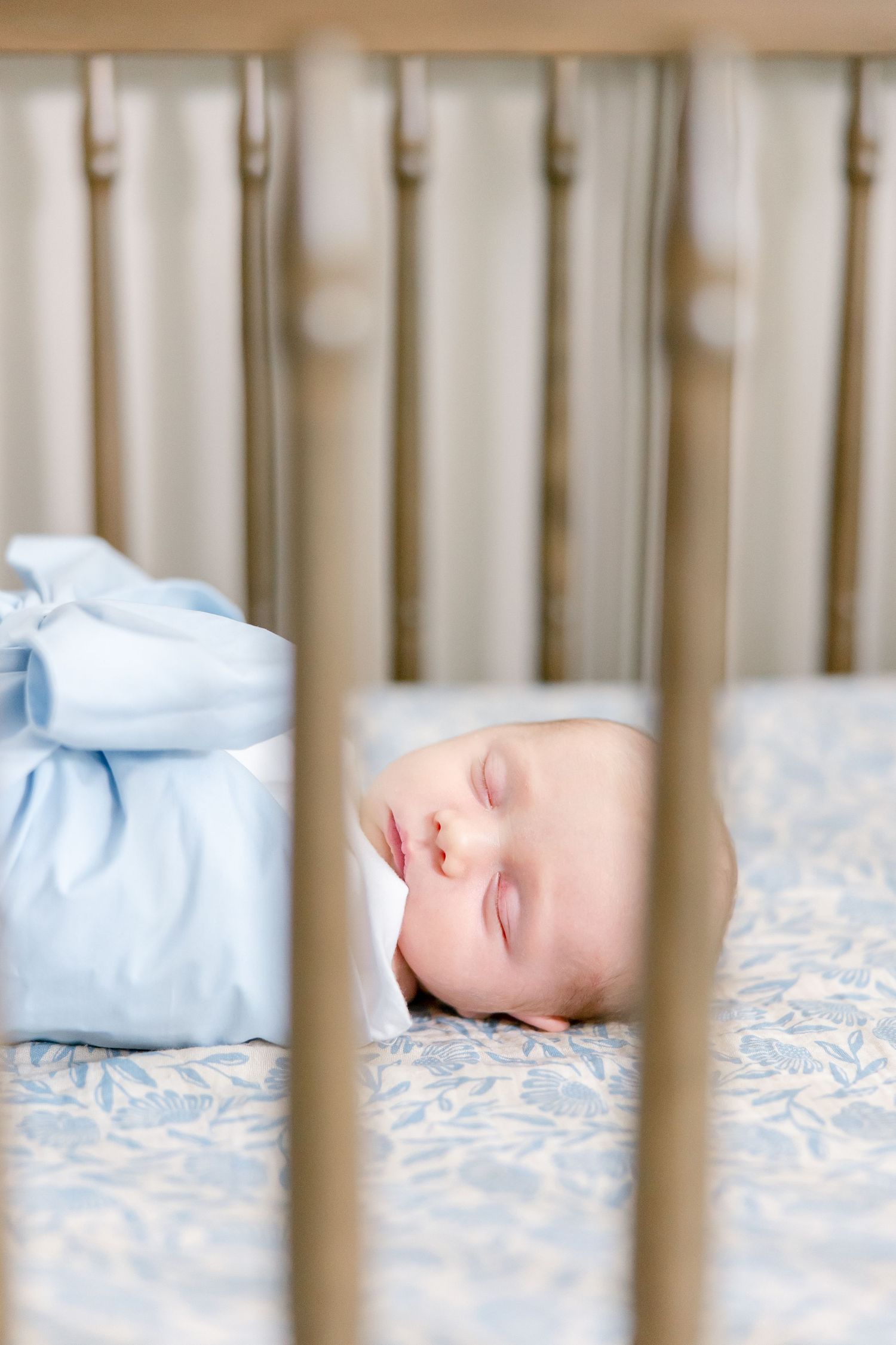 Peaceful baby sleeping soundly in light blue clothing against patterned bedding in wooden crib.