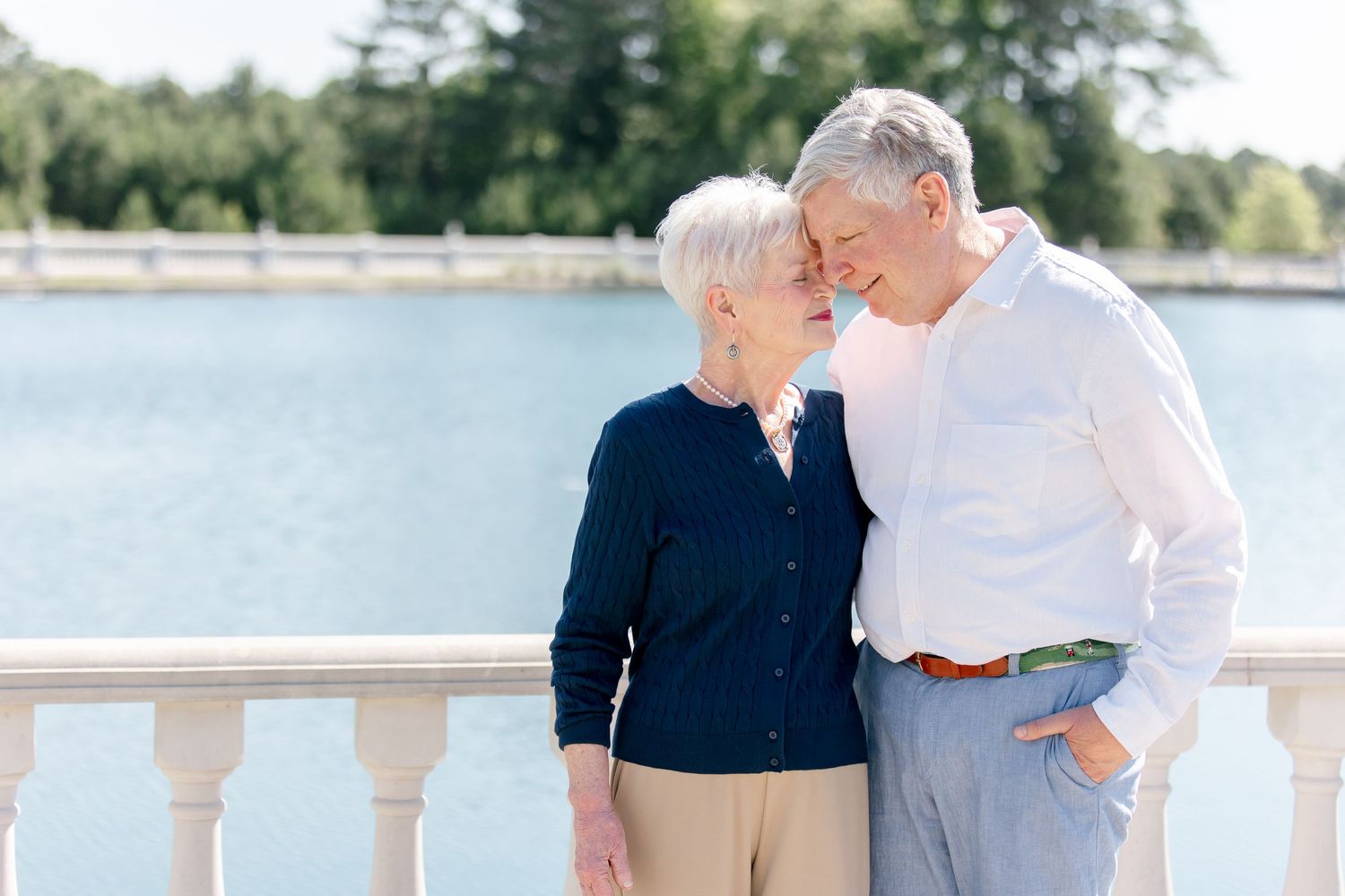 Tender moment between elderly couple embracing outdoors in romantic waterfront setting at dusk.