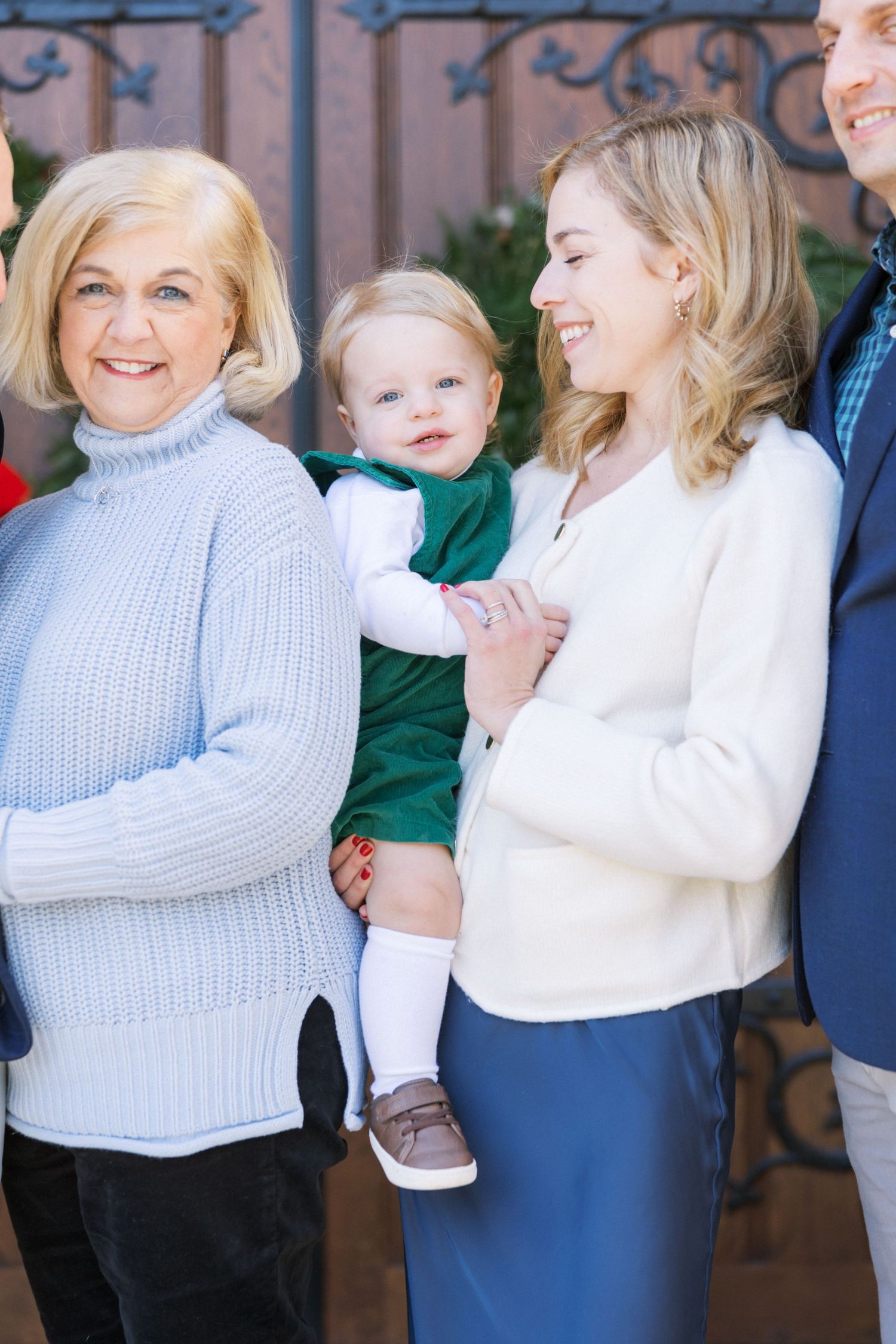 Multi-generational family portrait showing three adults and a small child in white and blue sweaters smiling together.