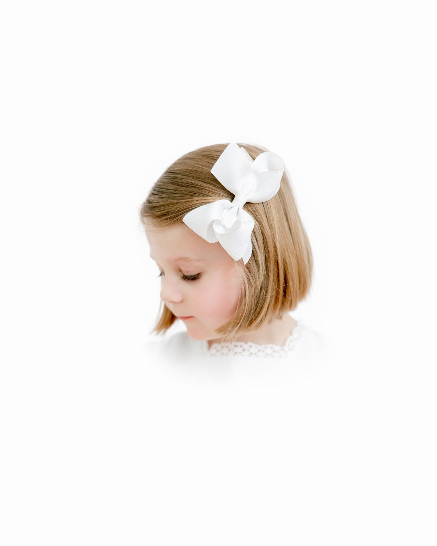 Side profile portrait of child wearing white bow against white background.